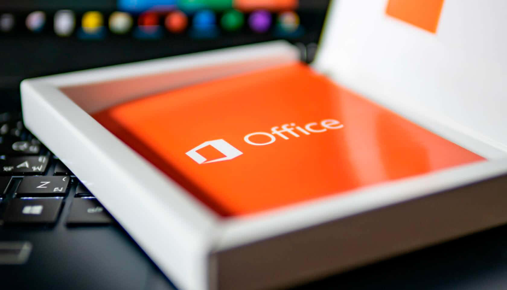 最大化 Office 365 的效能 壁紙 — 一個橙色Microsoft Office盒嘅特寫，放喺手提電腦鍵盤上面，背景有模糊嘅彩色圖示。