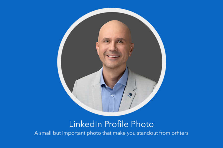 最大化你的 LinkedIn 簡介 壁紙 — 一位光頭男士穿著淺灰色西裝外套和藍色襯衫，在白色圓形框架內，對著純藍色背景溫暖地微笑。