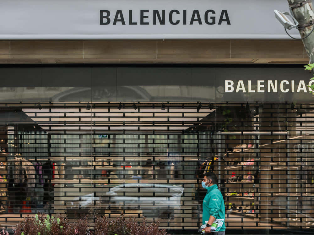 身穿青綠色襯衫和口罩的人走過 Balenciaga 商店，玻璃窗關閉。