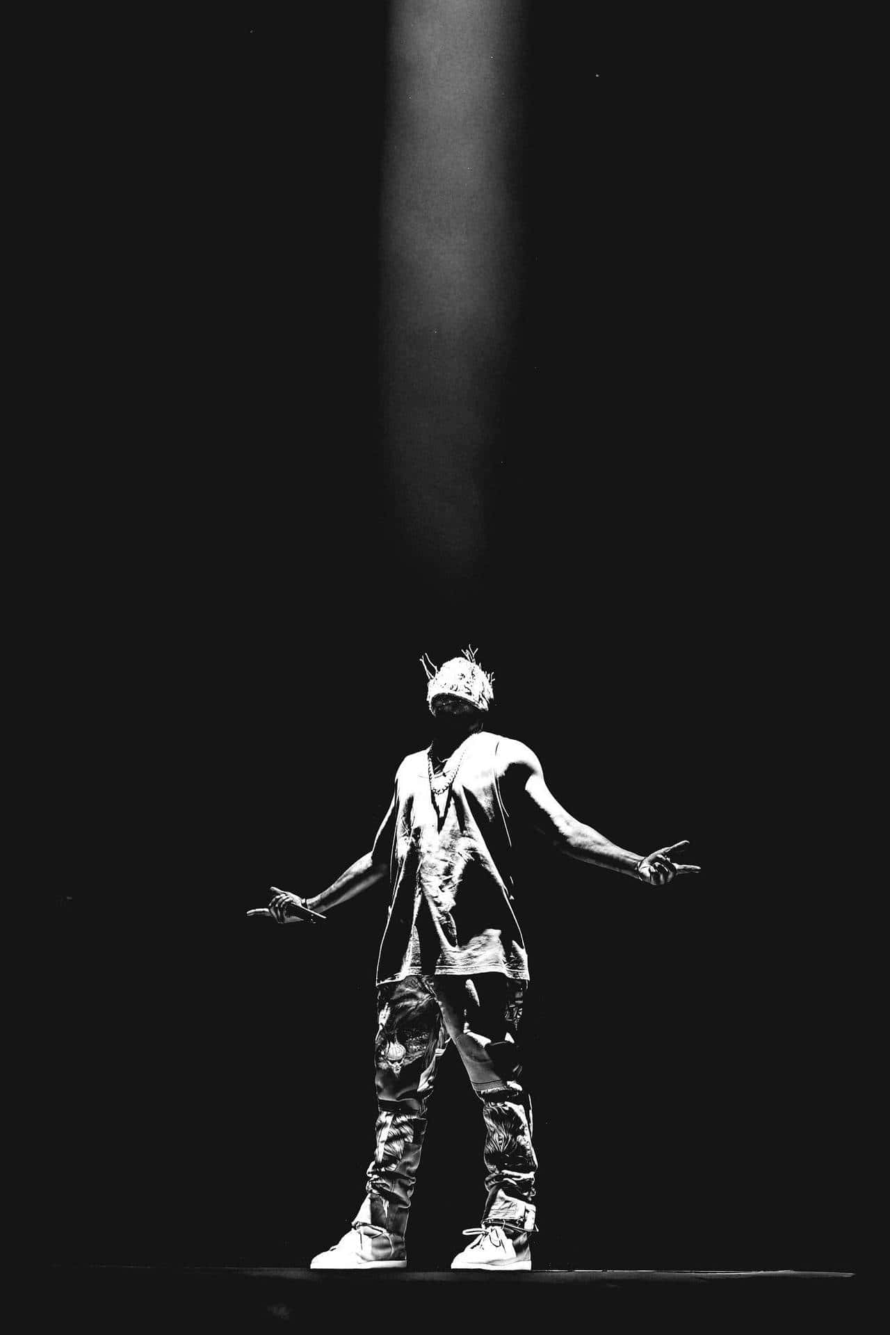 最新 Kanye West iPhone 特寫 壁紙 — 表演者站在舞台中央，單一聚光燈下，雙臂張開，形成戲劇性的黑白演唱會鏡頭。