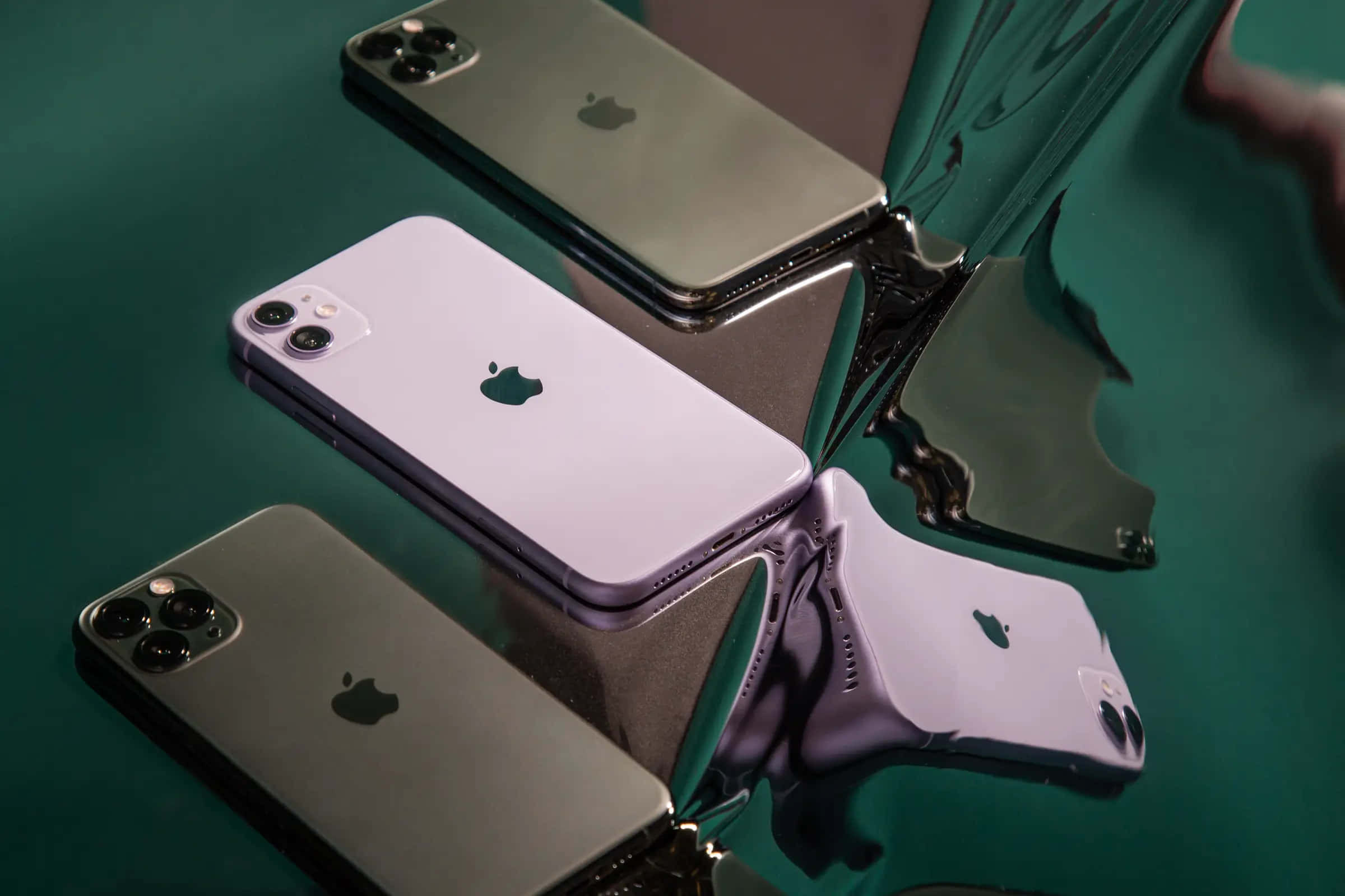 最新Apple智慧手機 壁紙 — 三部 Apple iPhone 分別為銀色、紫色和黑色，放置在帶有扭曲反射的亮綠色表面上。