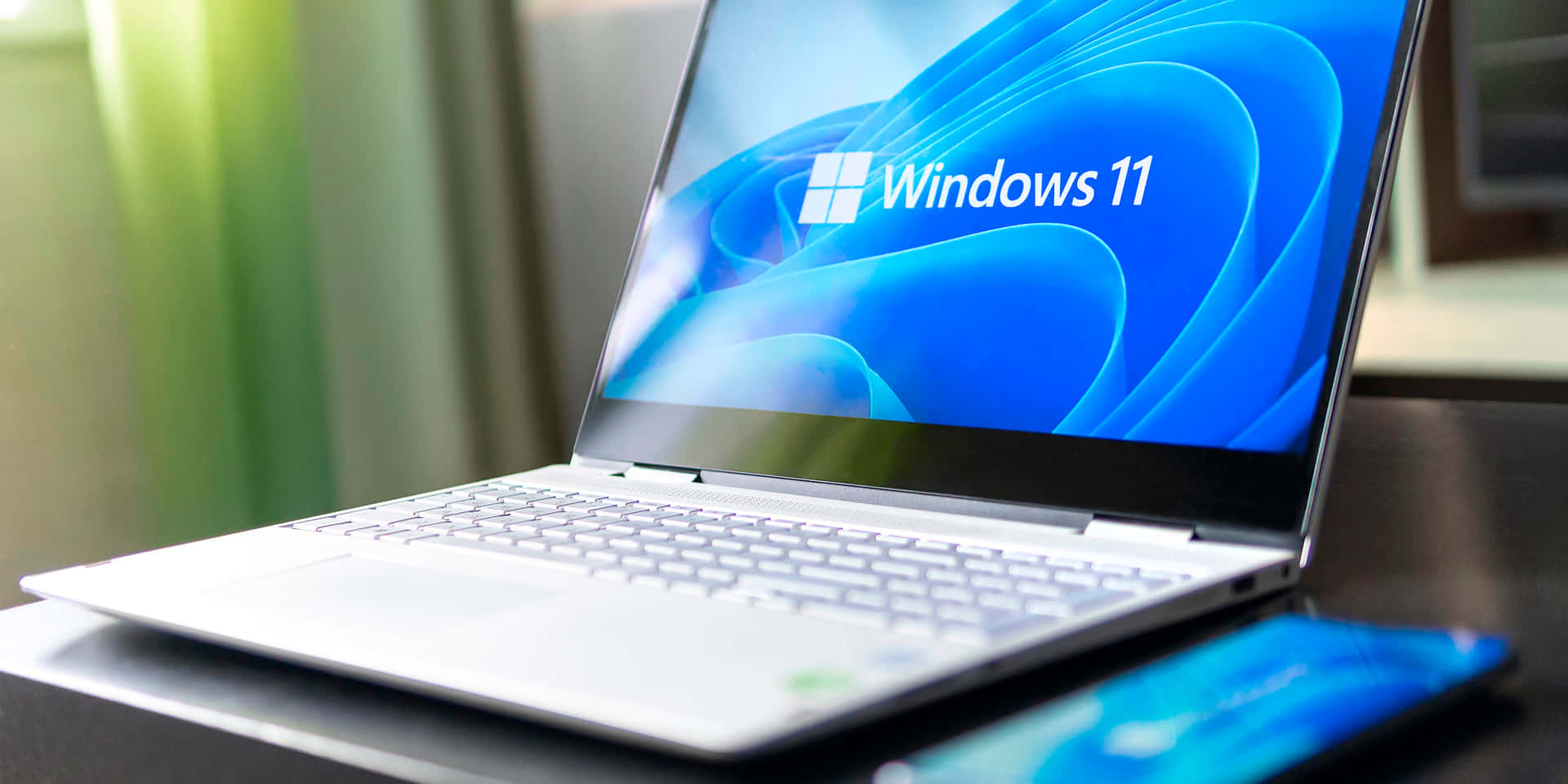 銀色手提電腦打開Windows 11畫面，放在深色桌子上，旁邊有智能手機。