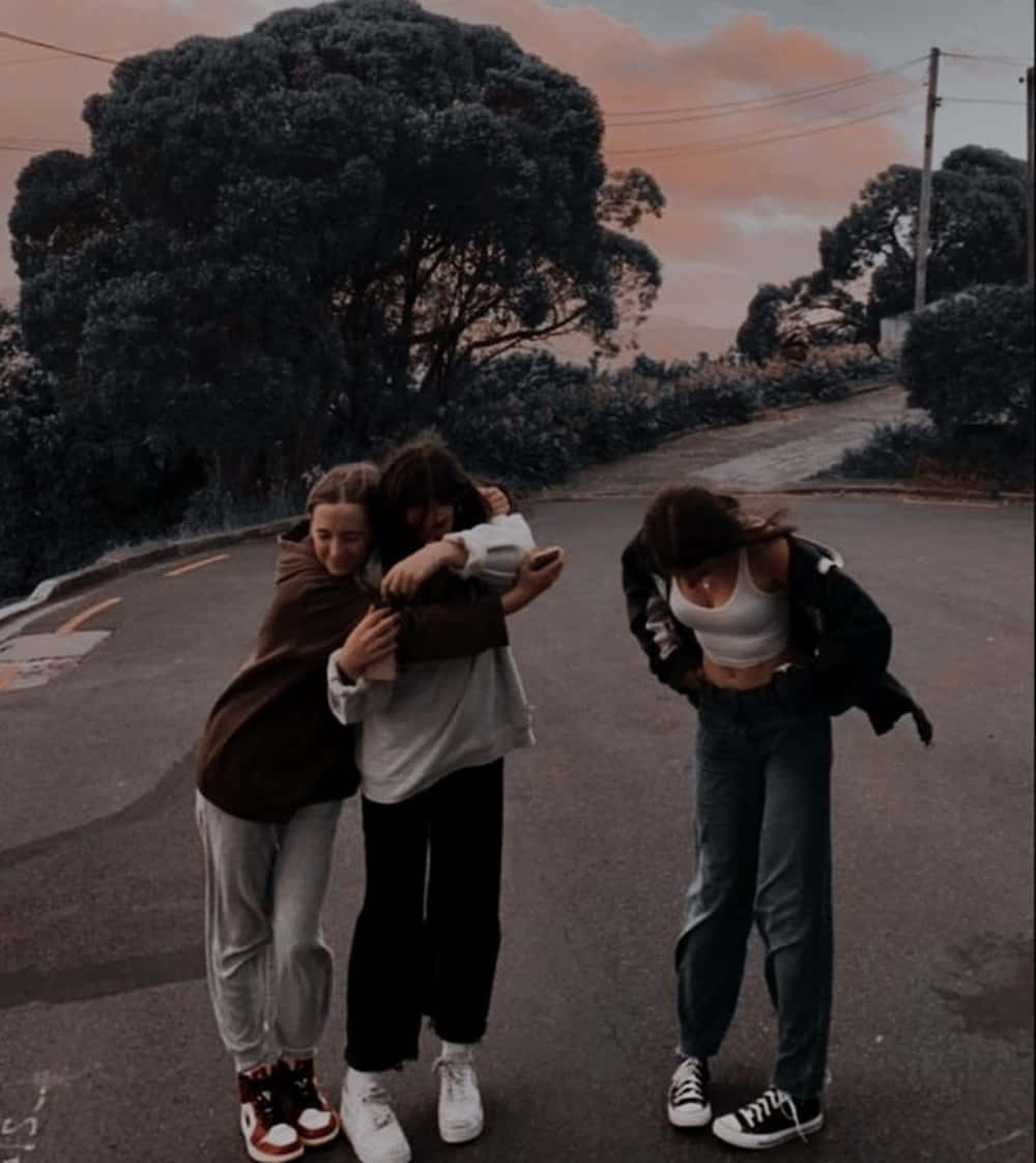 三個年輕朋友在日落時分的路上擁抱，天空呈現粉紅色和橙色