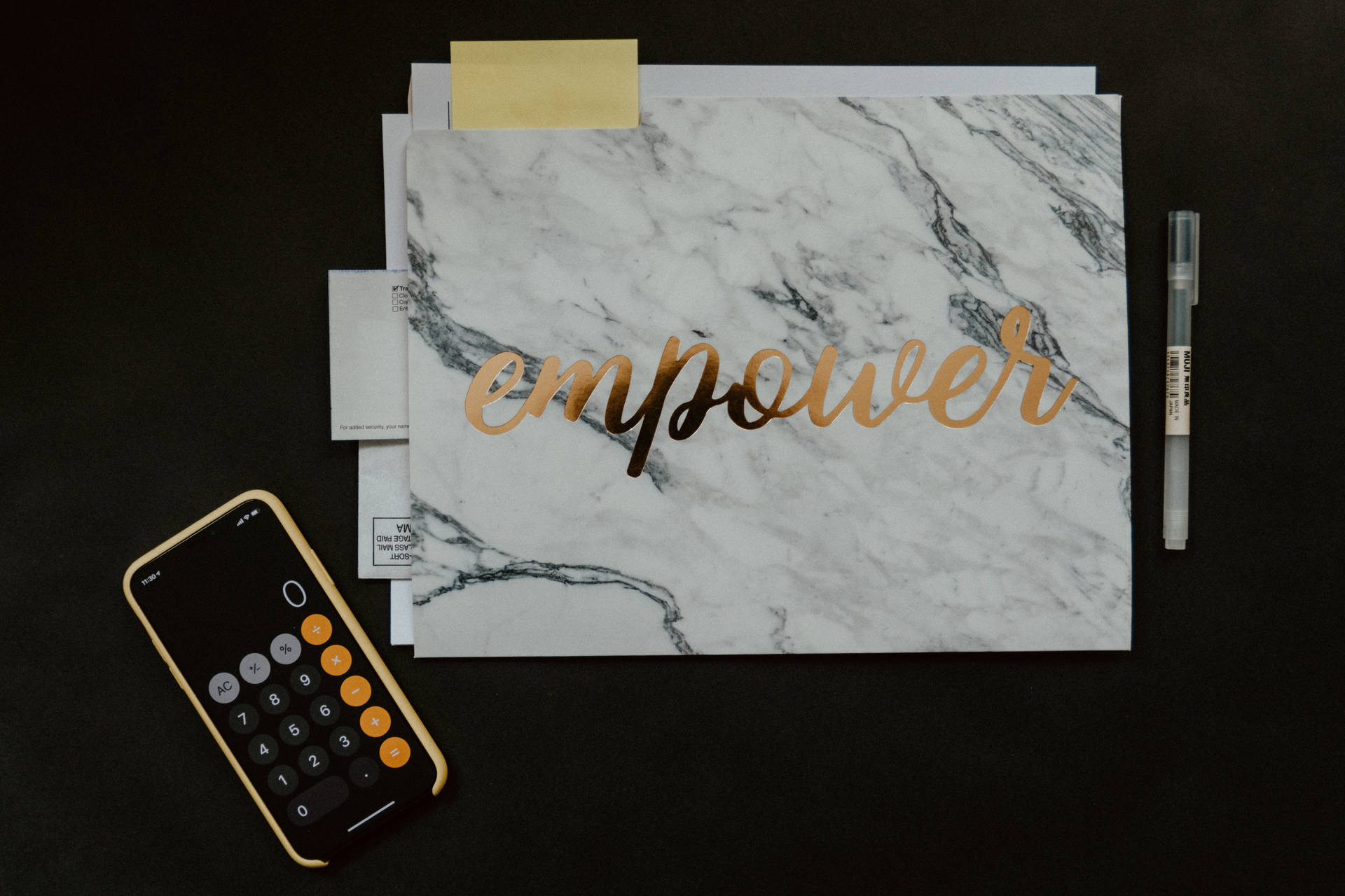 雲石文件夾帶金色箔片 'empower' 文字，旁邊有計算機和筆在黑色桌上。