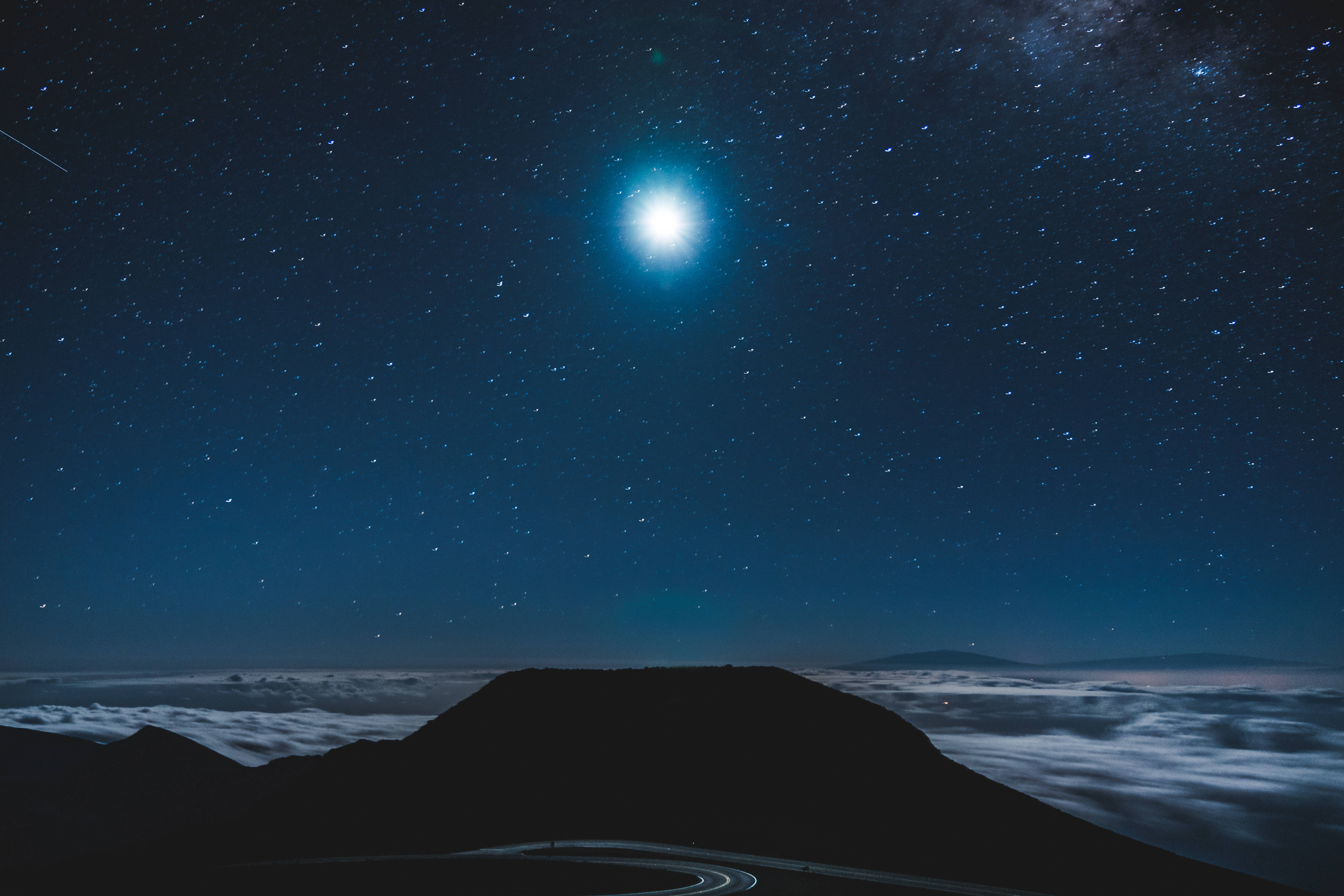 月亮與星系手機背景 壁紙 — 一條蜿蜒的道路在山頂上蜿蜒，上方是繁星點點的夜空，明亮的月亮和銀河。