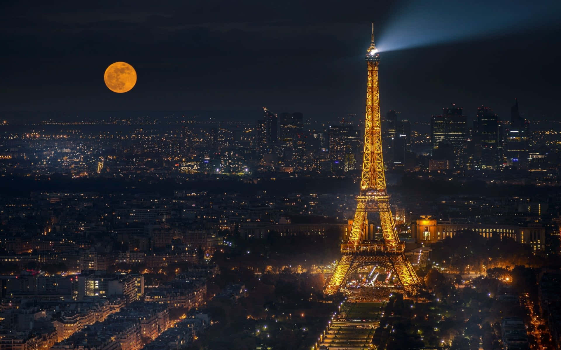 月光下的埃菲爾鐵塔夜景 壁紙 — 艾菲爾鐵塔在黑暗的天空中閃耀著金色光芒，滿月升起在巴黎屋頂和城市燈光之上。