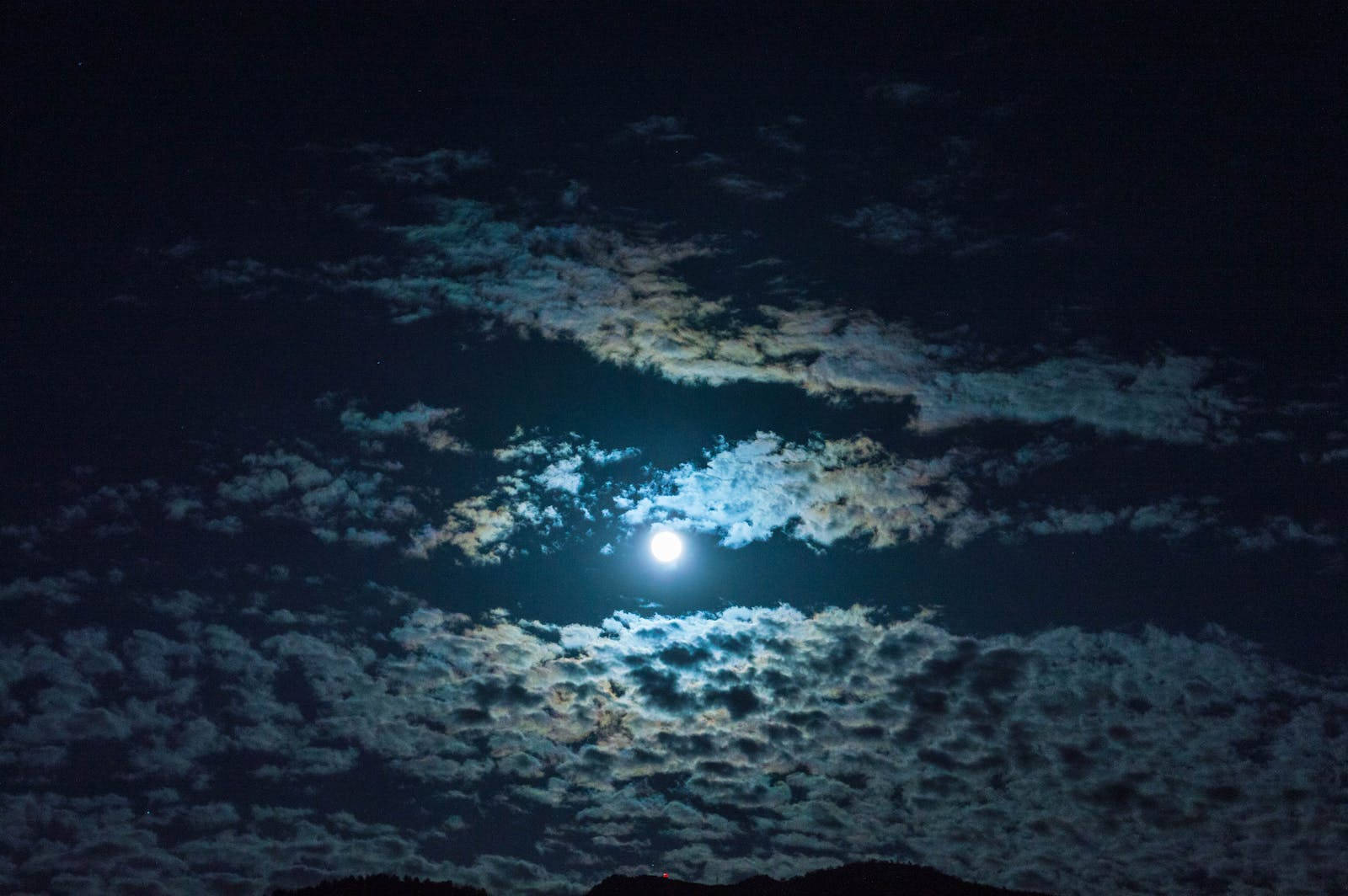 滿月在黑暗夜空中有紋理的雲層後發光。