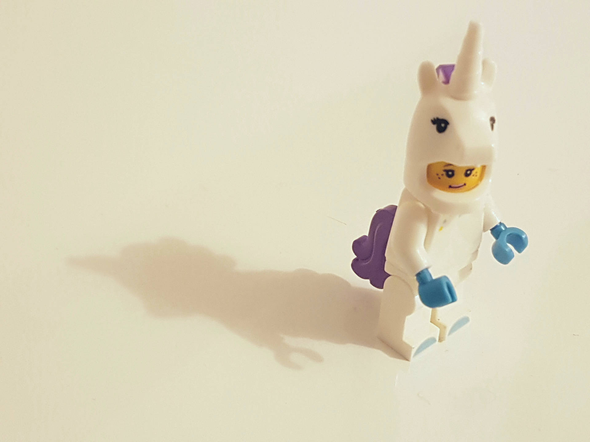 一個LEGO獨角獸迷你人偶，有紫色鬃毛和藍色手，站在純色表面。