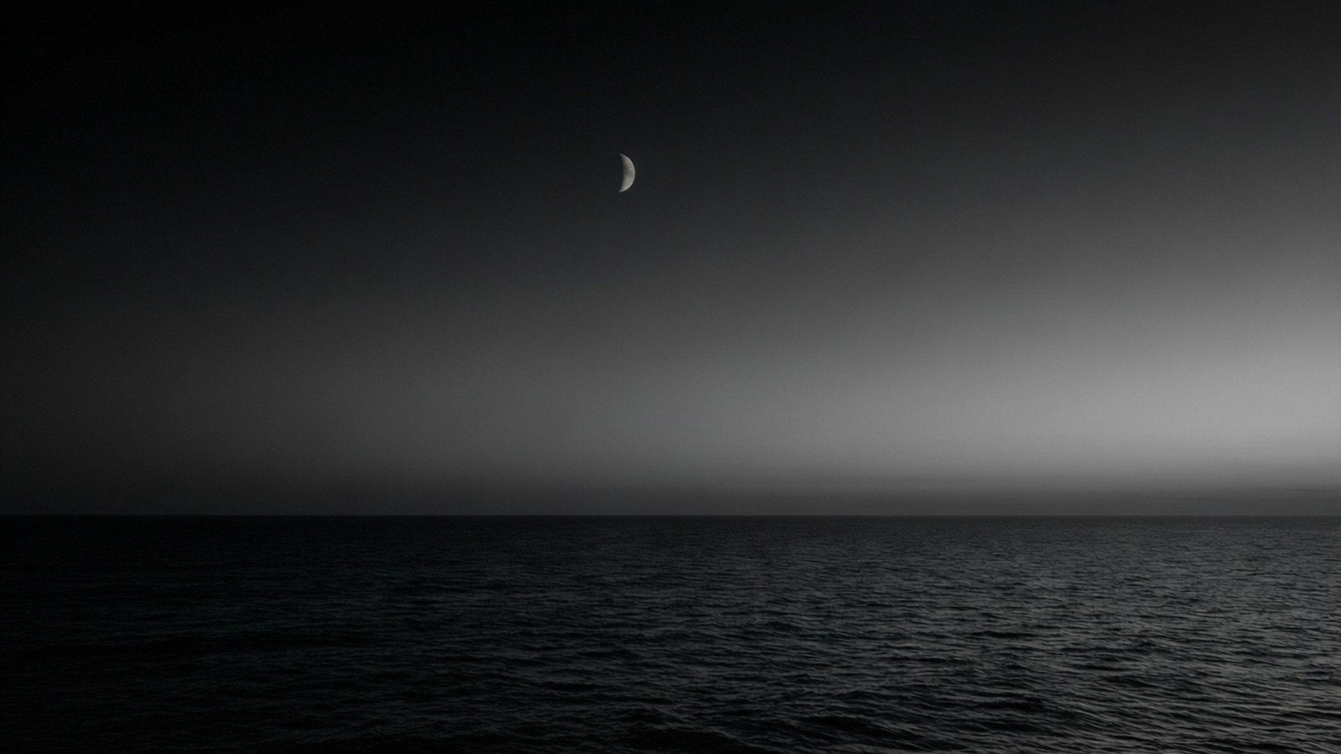 月光地平線 壁紙 — 寧靜的夜晚海景，一彎新月在漸變的天空下，柔和地照耀著平靜黑暗的水面。