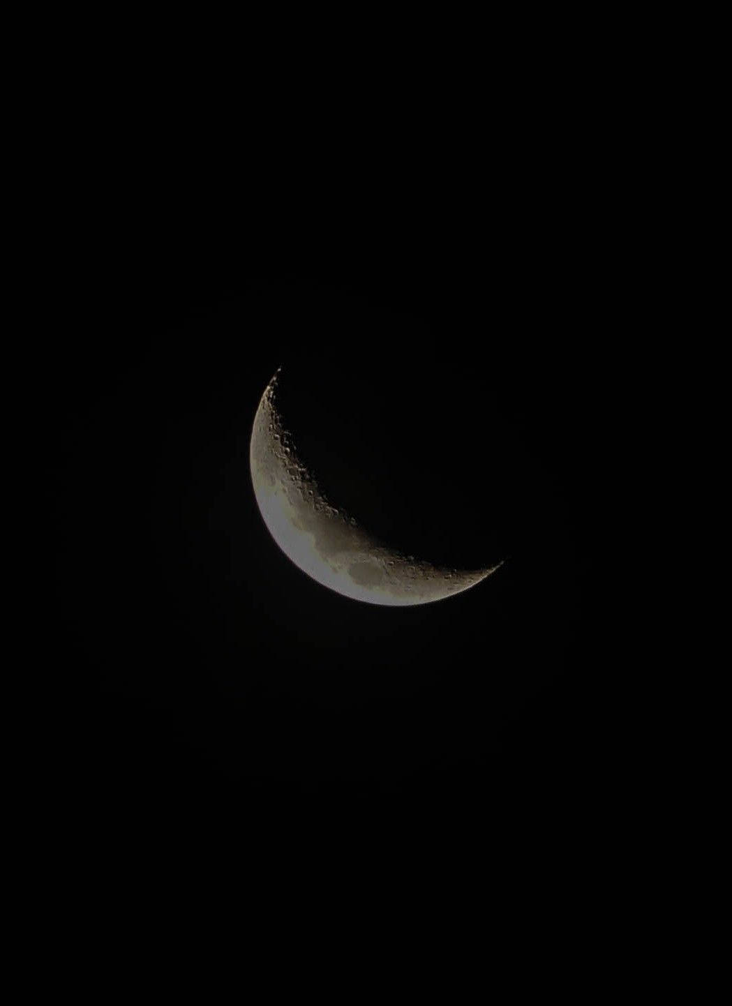 在黑暗的夜空中，帶有可見隕石坑的月牙。