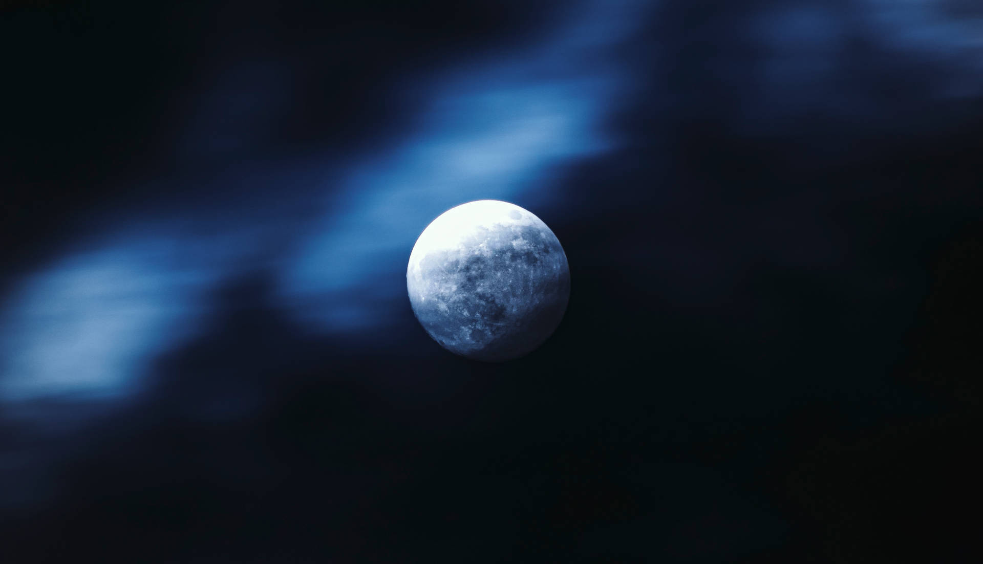 滿月在夜間透過深藍色雲層閃耀。