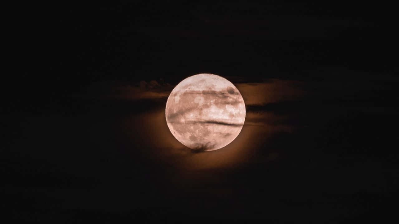 月光穿雲 壁紙 — 一輪明亮的滿月穿過薄雲，在深邃的黑色夜空中溫暖地發光。