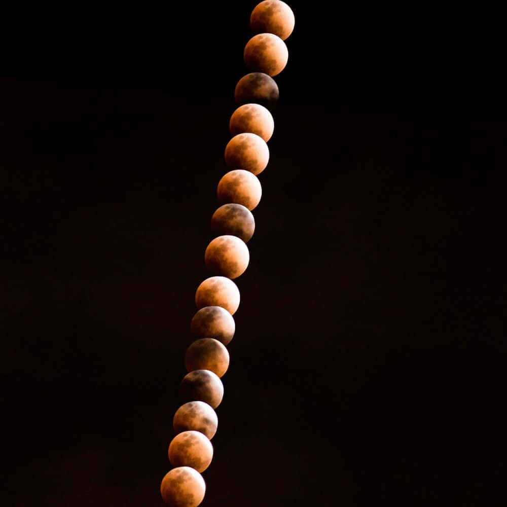 Moon Phases 桌布 壁紙 — 月全食期間月球階段的垂直序列，在漆黑天空中發出琥珀色光芒。