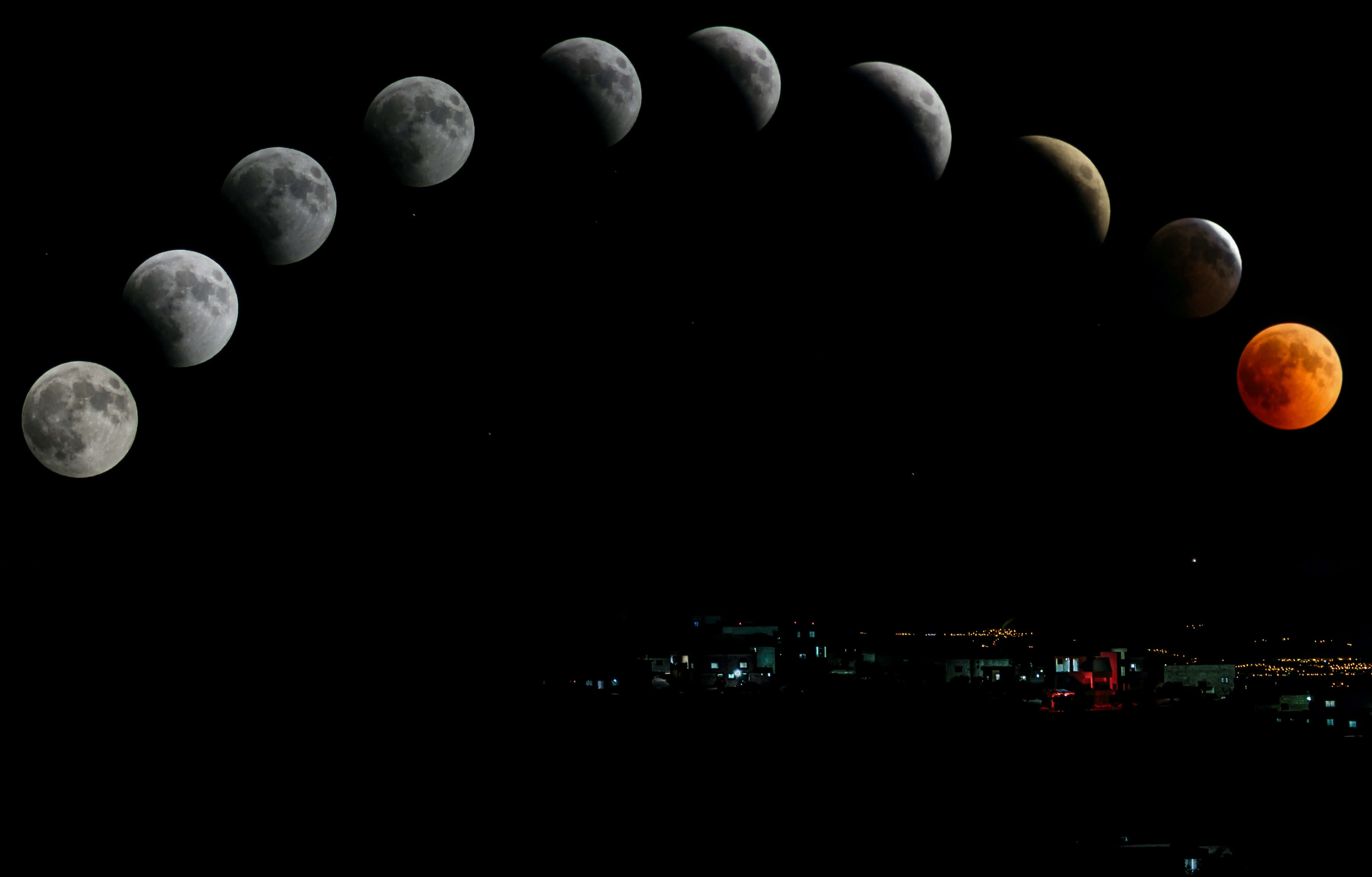 月相城市夜景圖 壁紙 — 一個戲劇性的月食序列在夜空中拱起，下方是剪影般的城市景觀，燈光閃爍。