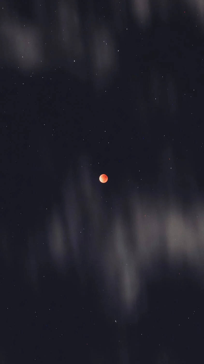 月蝕黑星 壁紙 — 一輪發光的橙色月亮懸掛在繁星點點的夜空，部分被柔和飄動的雲層遮蓋。