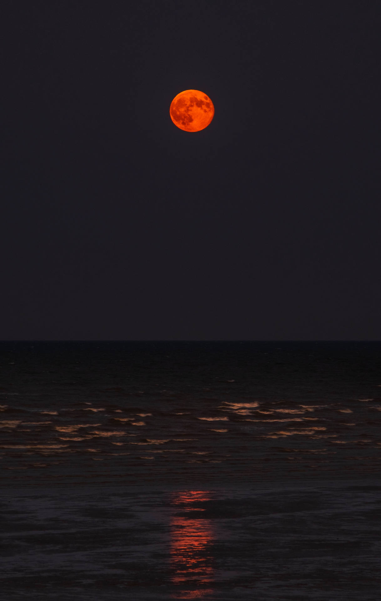 一輪明亮的橙色滿月反射在黑暗的海浪上，背景是夜空。