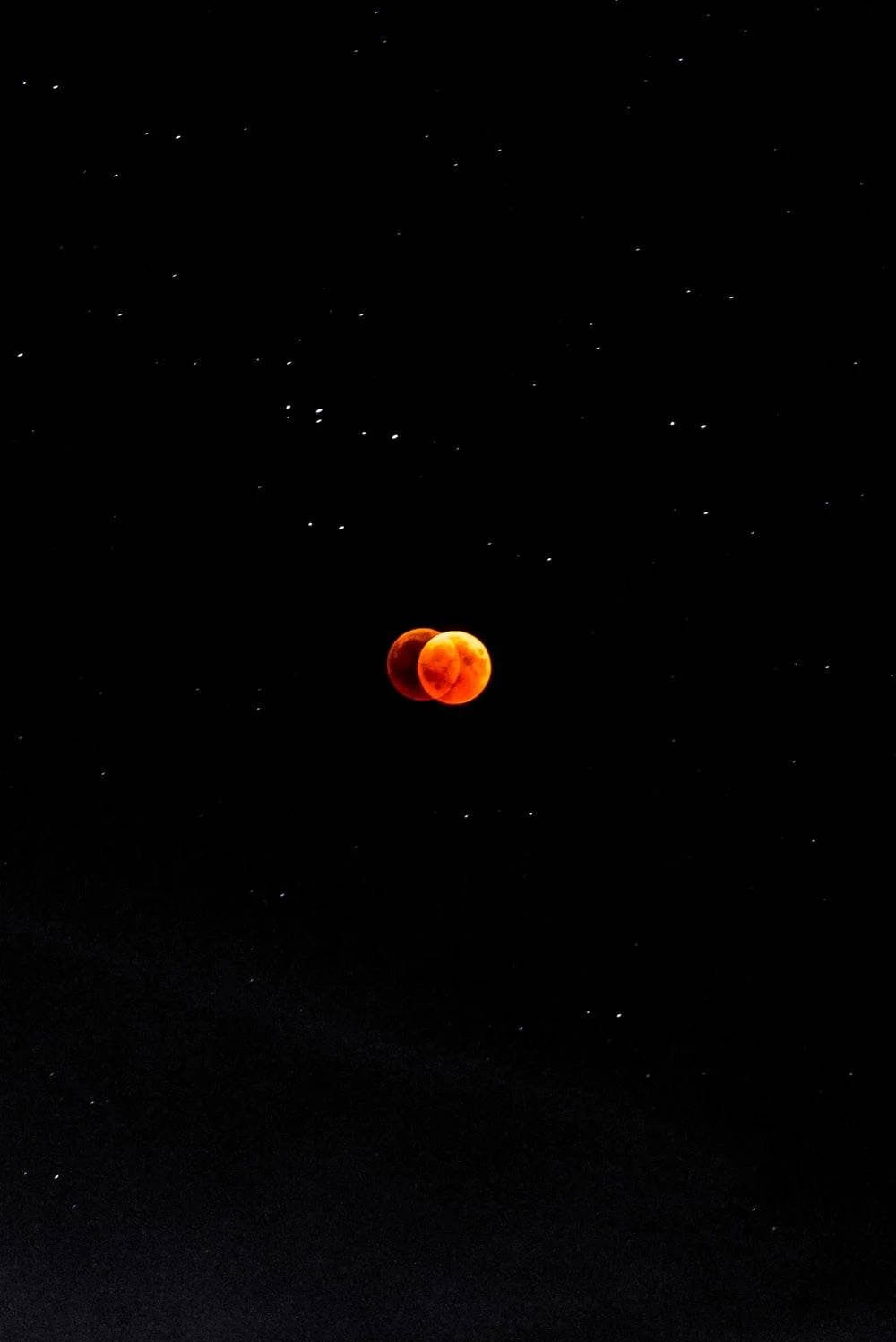 月食肖像 壁紙 — 被陰影遮蔽的血月，在繁星點點的夜空中發出火橙色光芒。