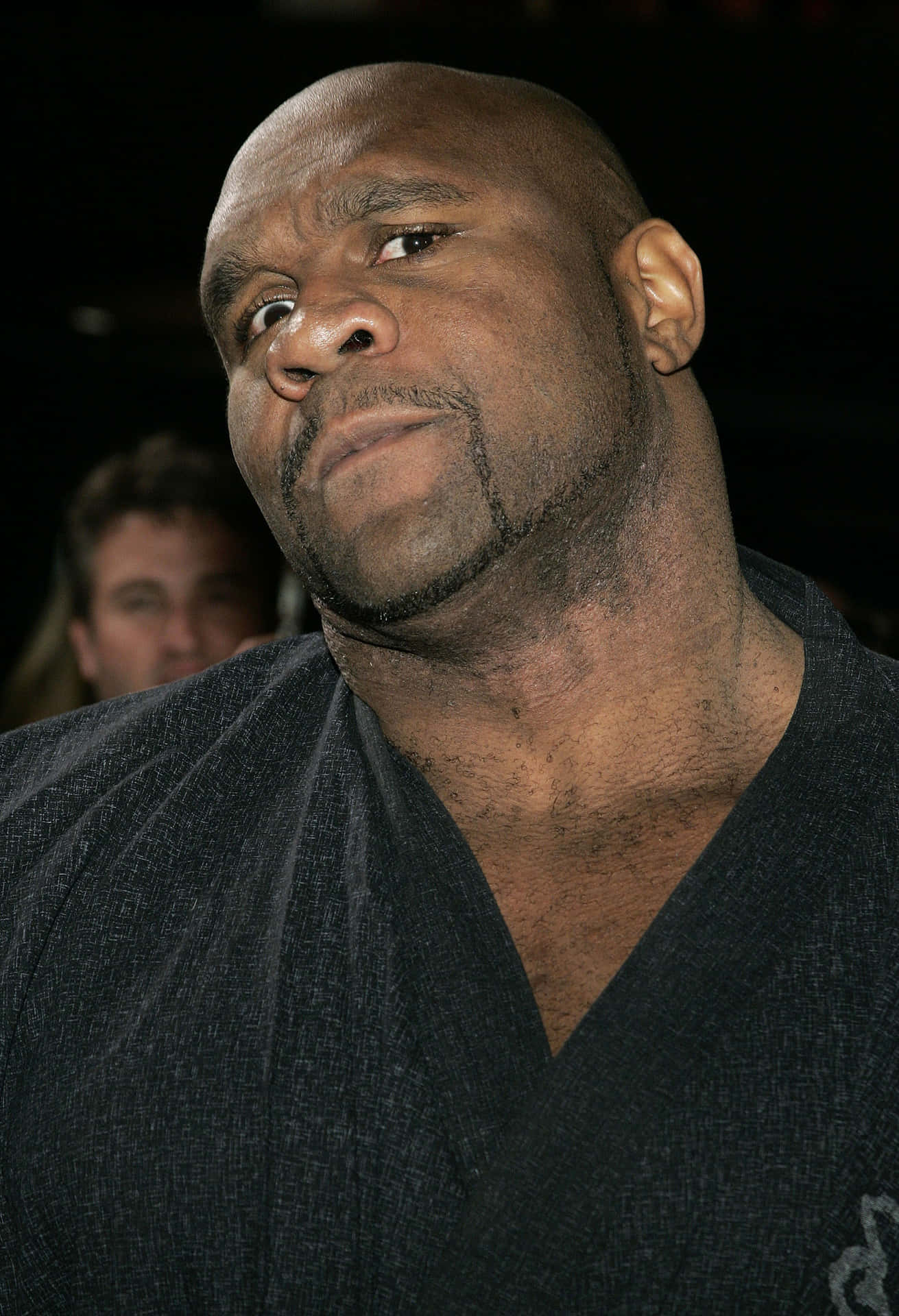 有趣可愛的 Bob Sapp 壁紙 — 特寫肖像，一名光頭黑人男子表情嚴肅，身穿深色紋理襯衫，背景模糊。