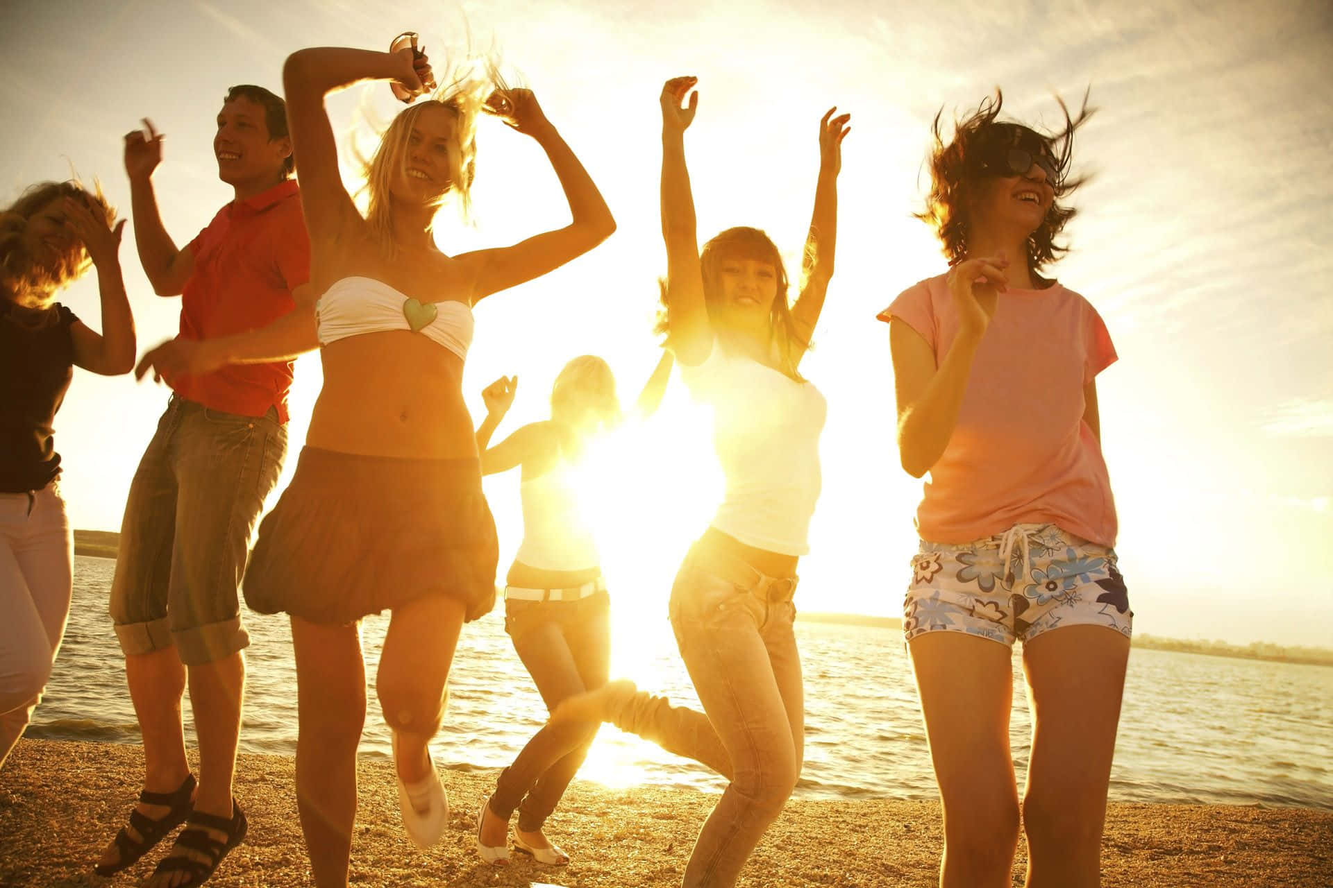 Beach Dance Party 桌布 壁紙 — 朋友們在海灘上快樂地跳舞，金色的夕陽光芒在他們身後閃耀。