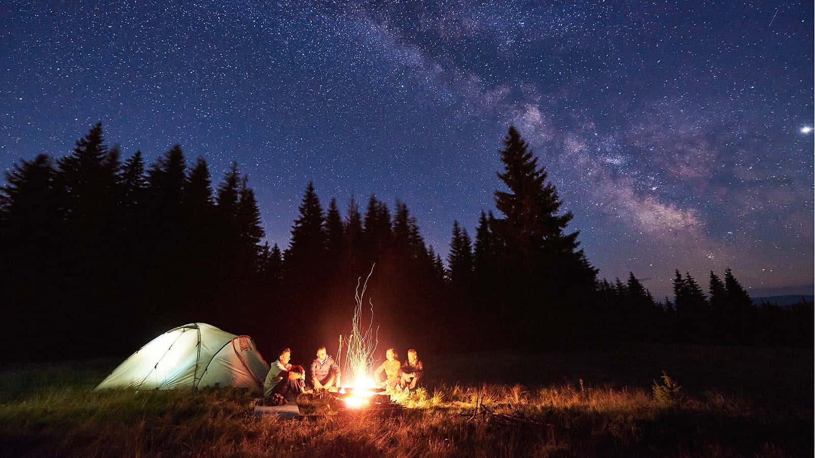一群朋友在星空下享受營火，銀河清晰可見。