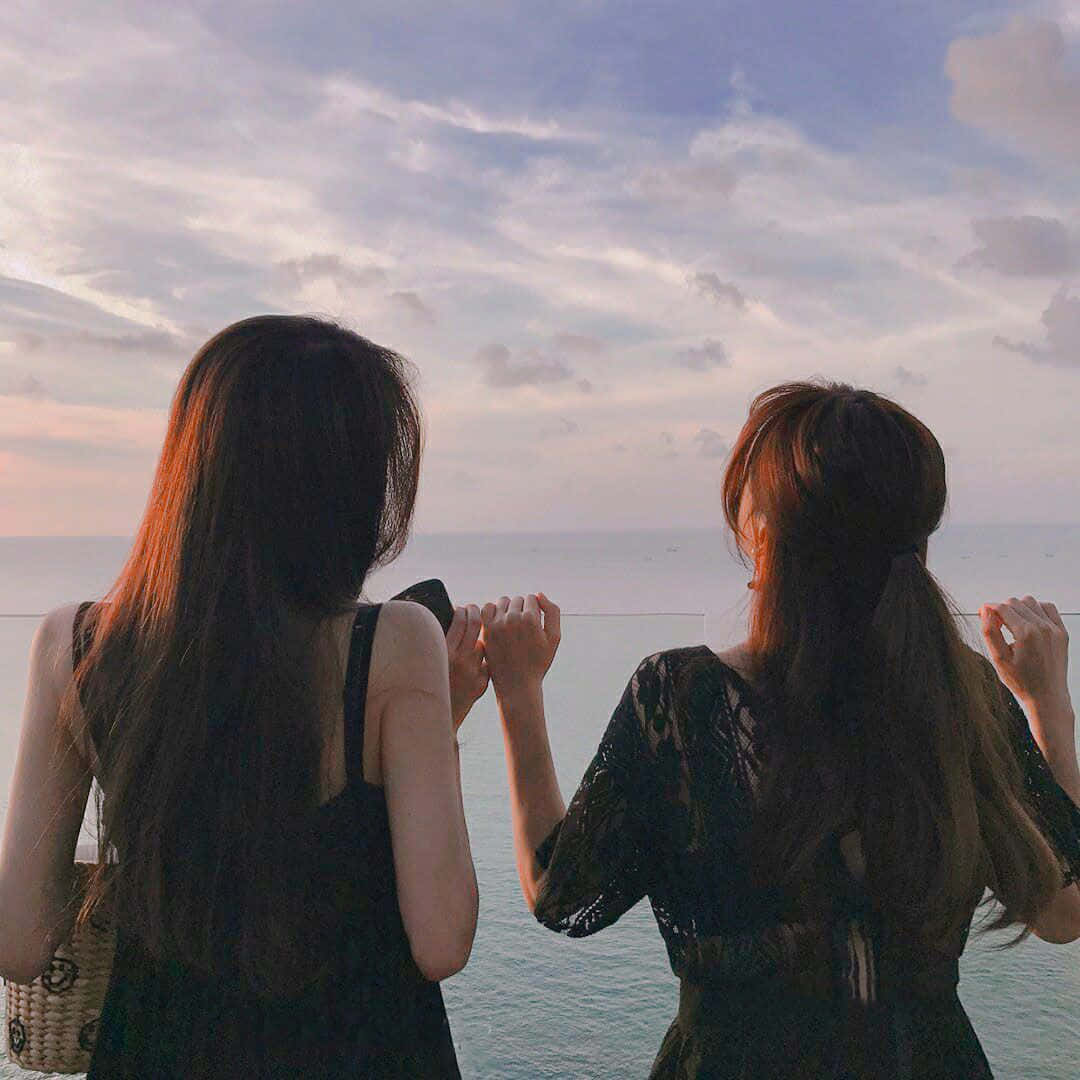 兩位女士手牽手在日落時觀看海洋。