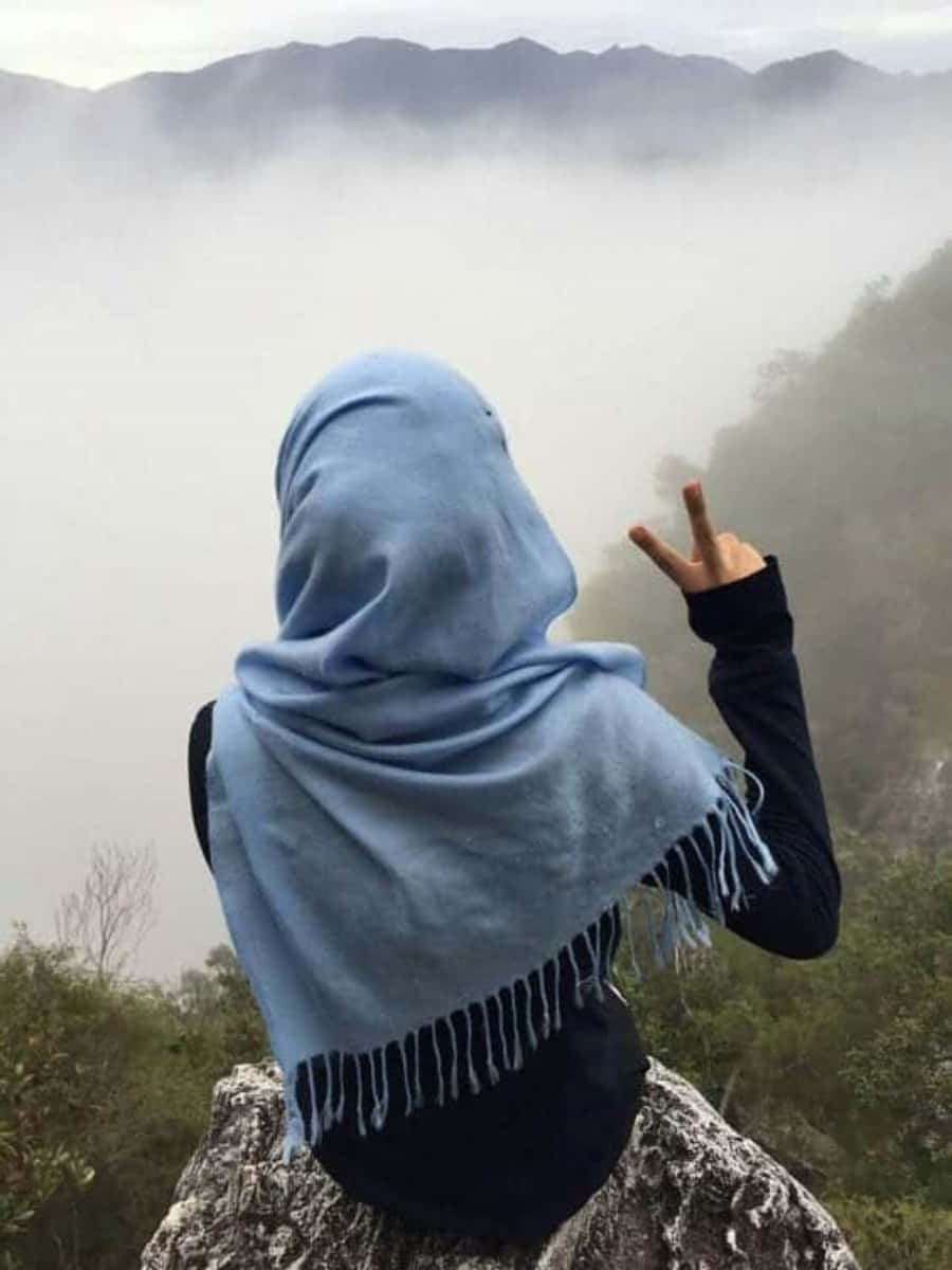 藍色頭巾人士在山崖上做出和平手勢，下方是霧谷