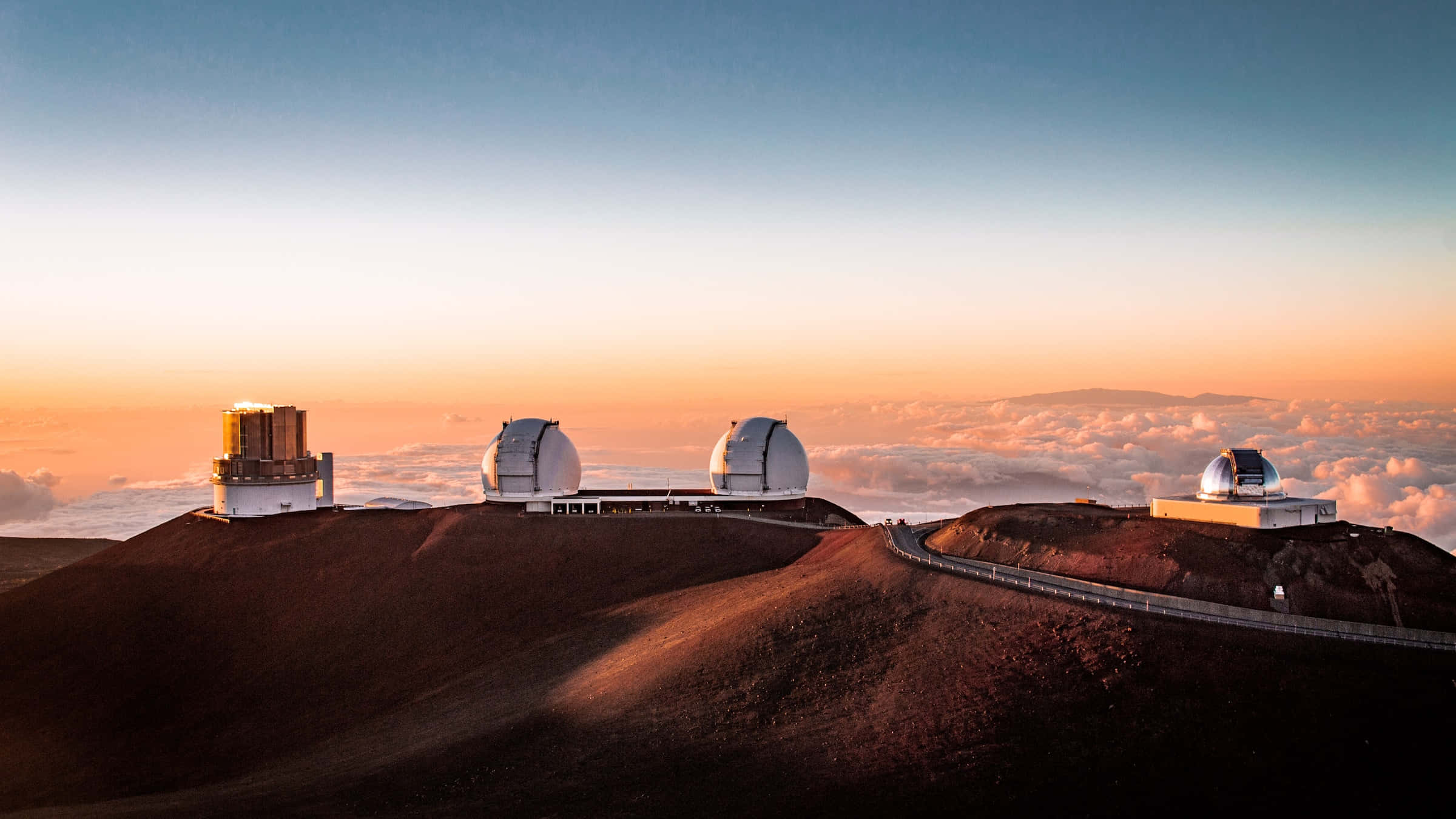 Space Observation 桌布 壁紙 — 望遠鏡圓頂棲息在火山脊上，日出時將溫暖的光線投射到下方的雲海之上。