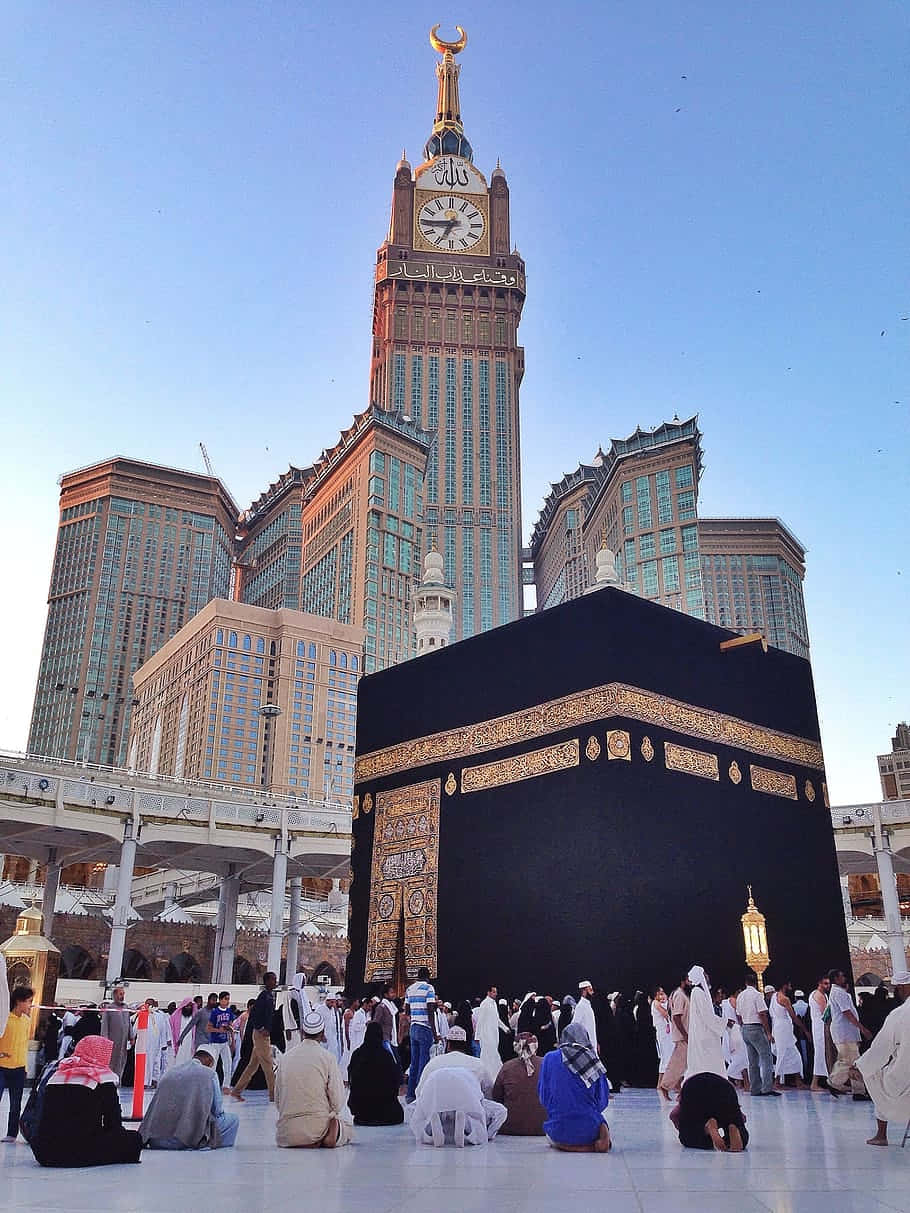 Makkah 桌布 壁紙 — 朝聖者在晴朗的藍天下圍繞天房祈禱，背後的阿布拉吉阿爾拜特鐘樓高聳入雲。