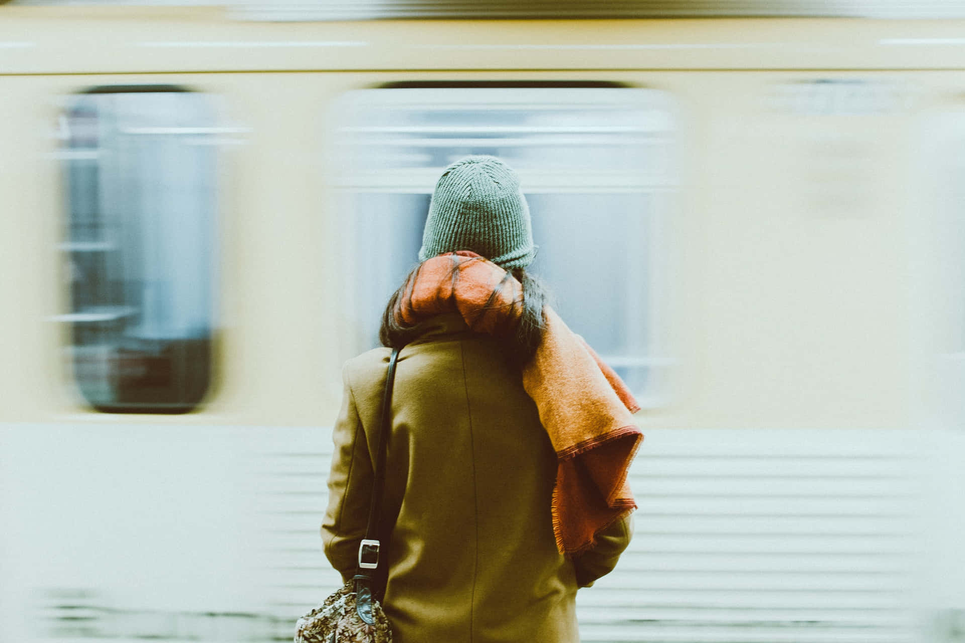 戴著帽子和外套的人在火車站等待經過的火車。