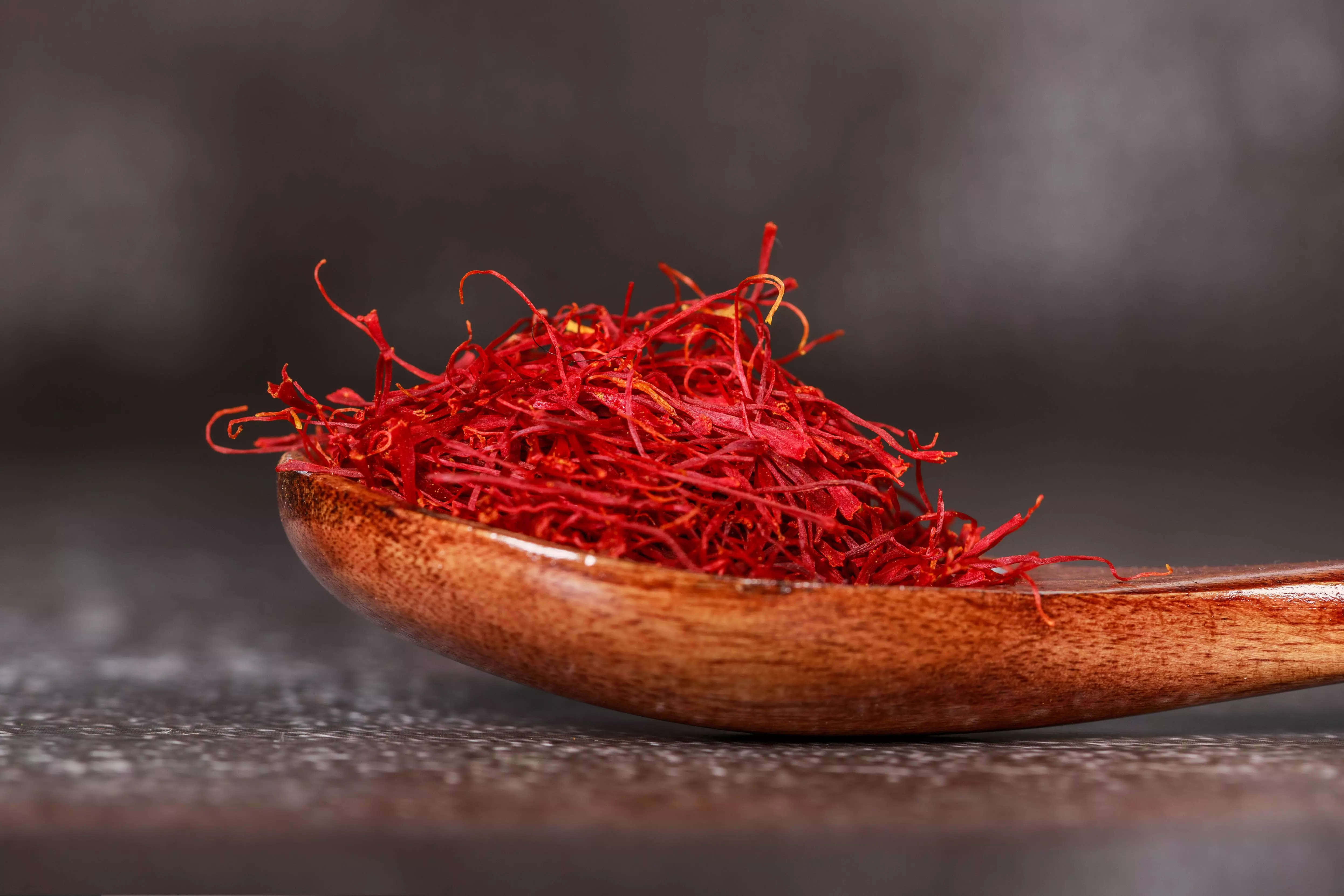 Saffron 桌布 壁紙 — 木勺盛著鮮紅的藏紅花絲，背景是深色模糊的。