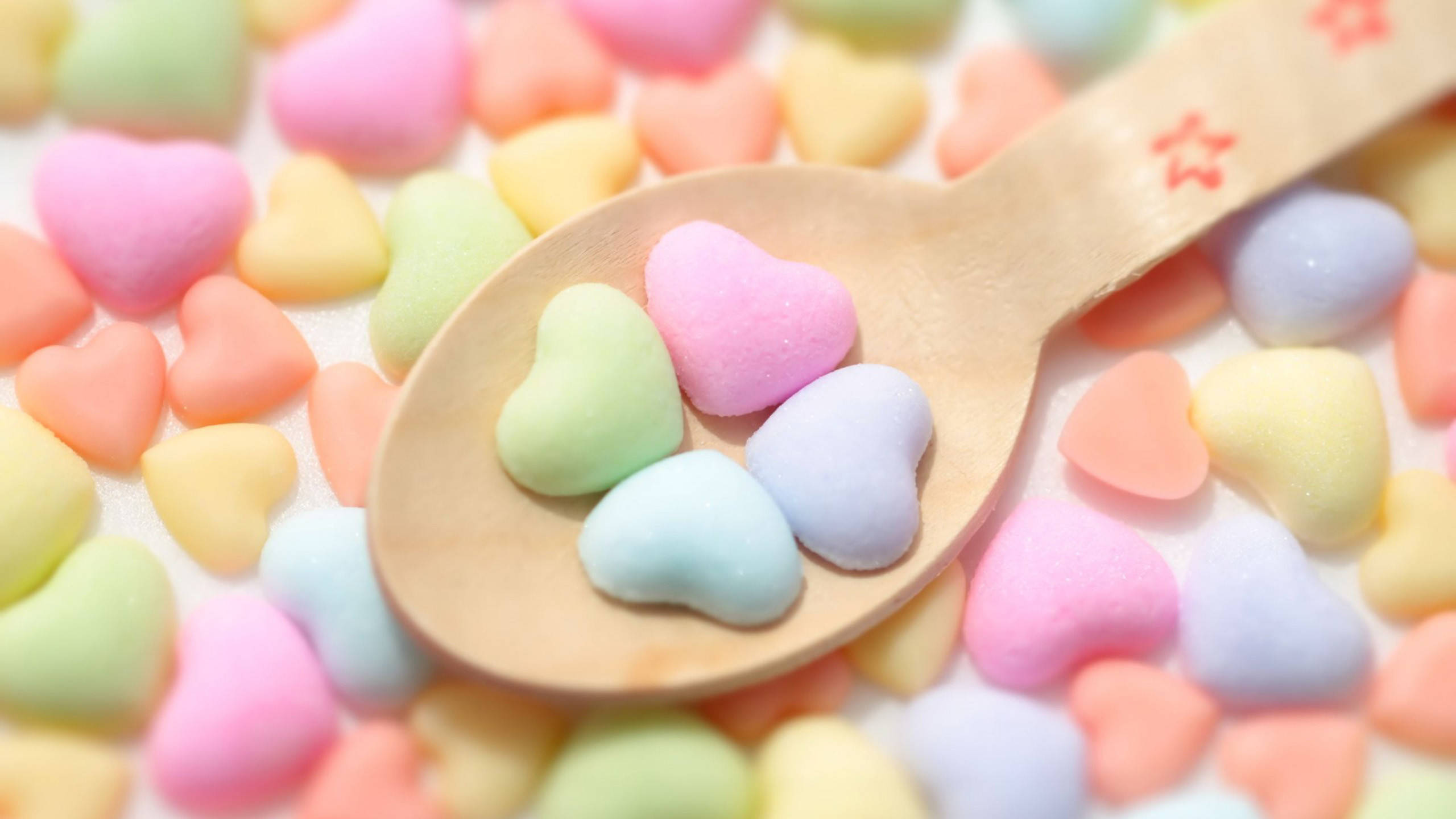 Marshmallow 桌布 壁紙 — 木匙盛載著粉彩色心形糖果，周圍是色彩繽紛散落的背景。