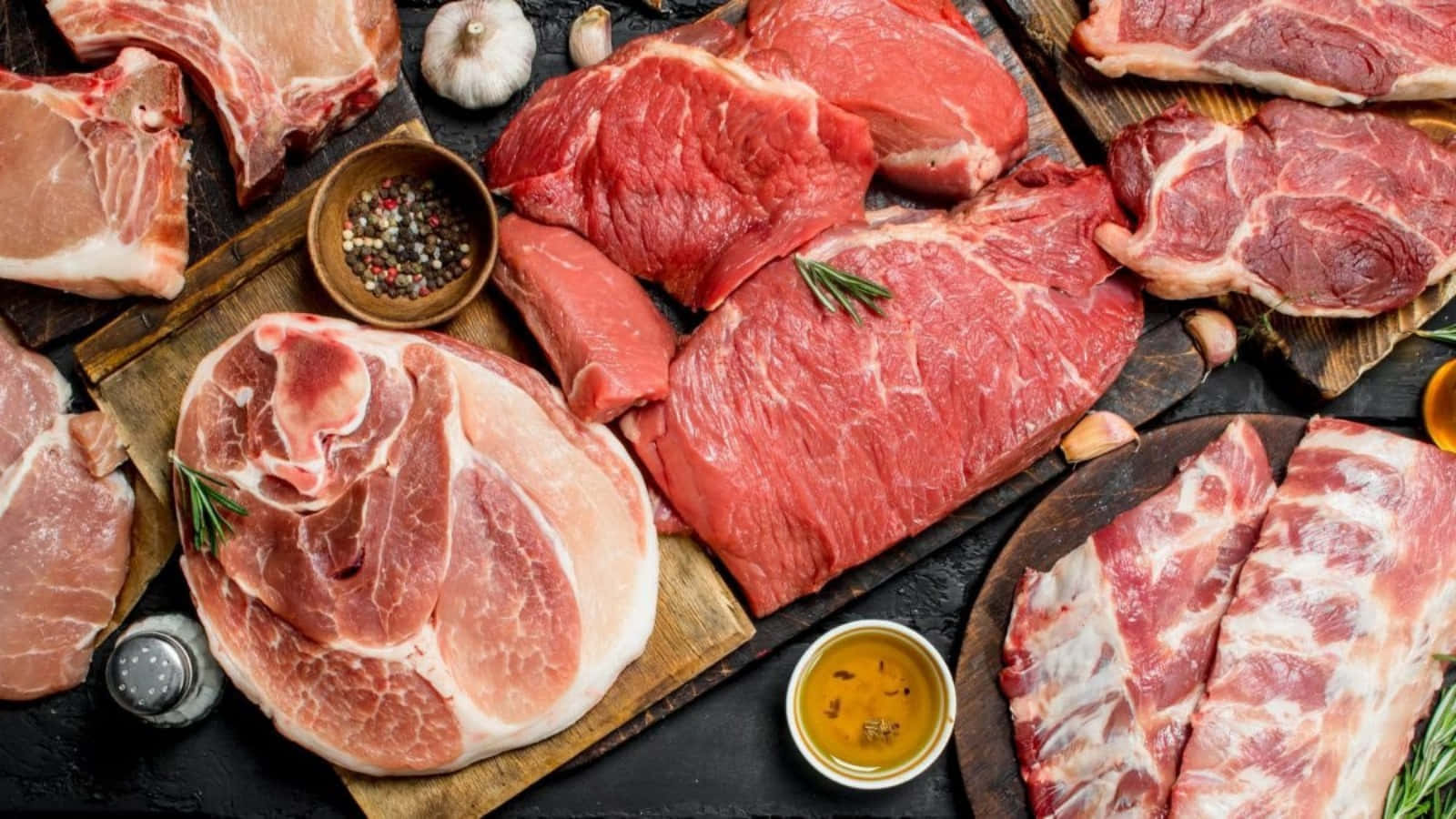 meat 桌布 壁紙 — 木板上擺放著各種生紅肉和豬肉塊，配上大蒜、迷迭香和油，呈現質樸的擺盤。