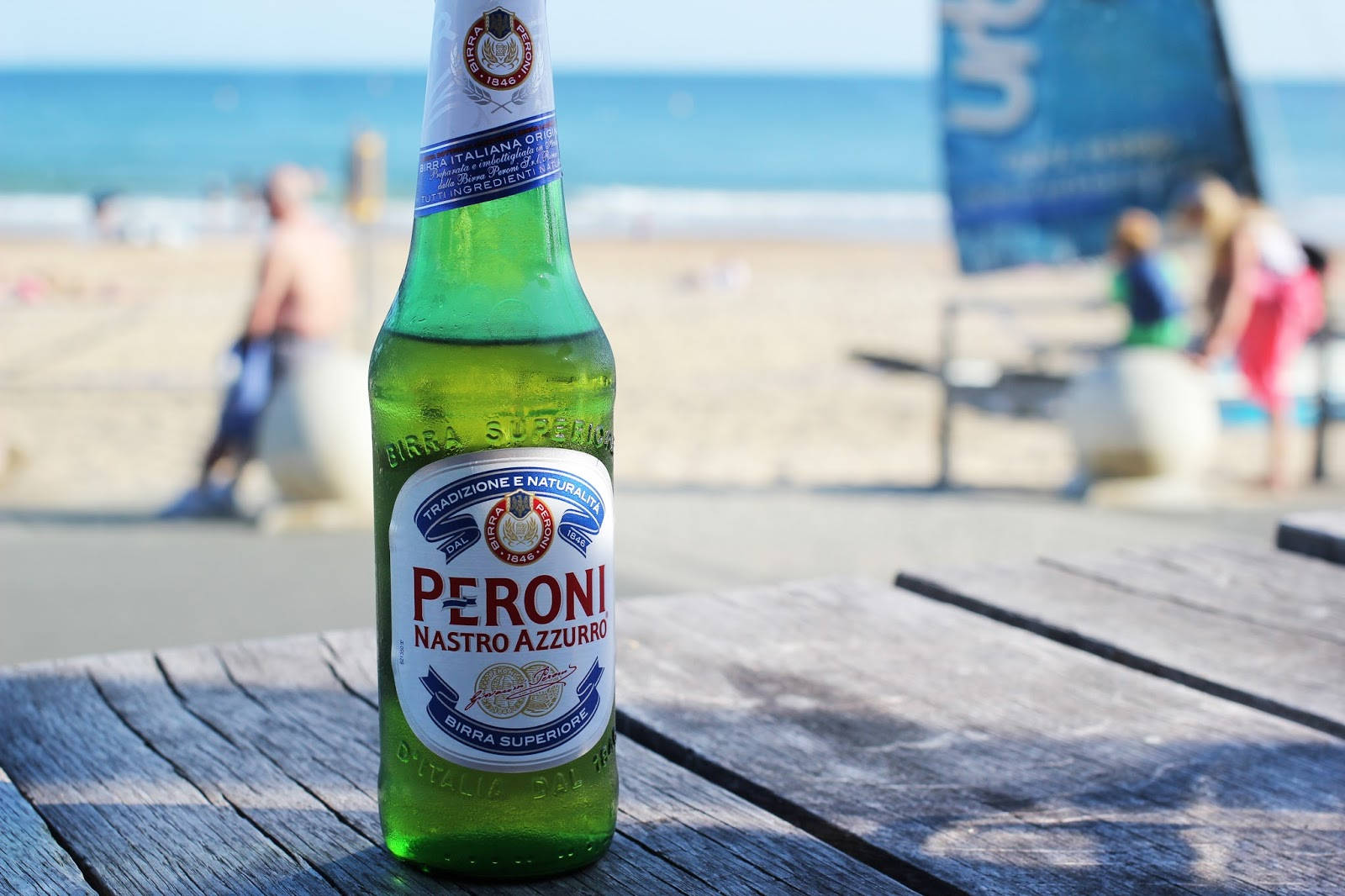 陽光海灘木桌上的綠色 Peroni 啤酒瓶