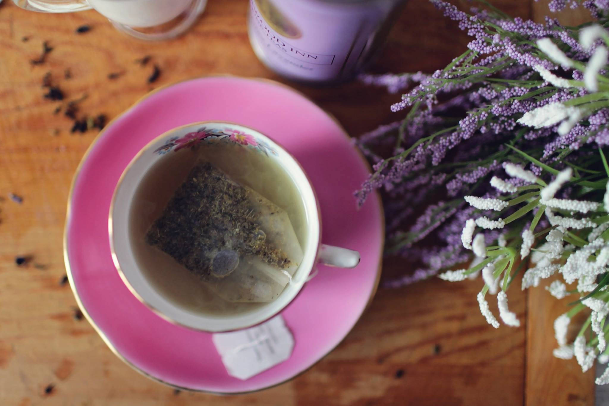 咖啡 桌布 壁紙 — 木桌上粉紅色茶杯俯視圖，旁邊有浸泡中的草本茶包，以及一束紫色和白色的花。