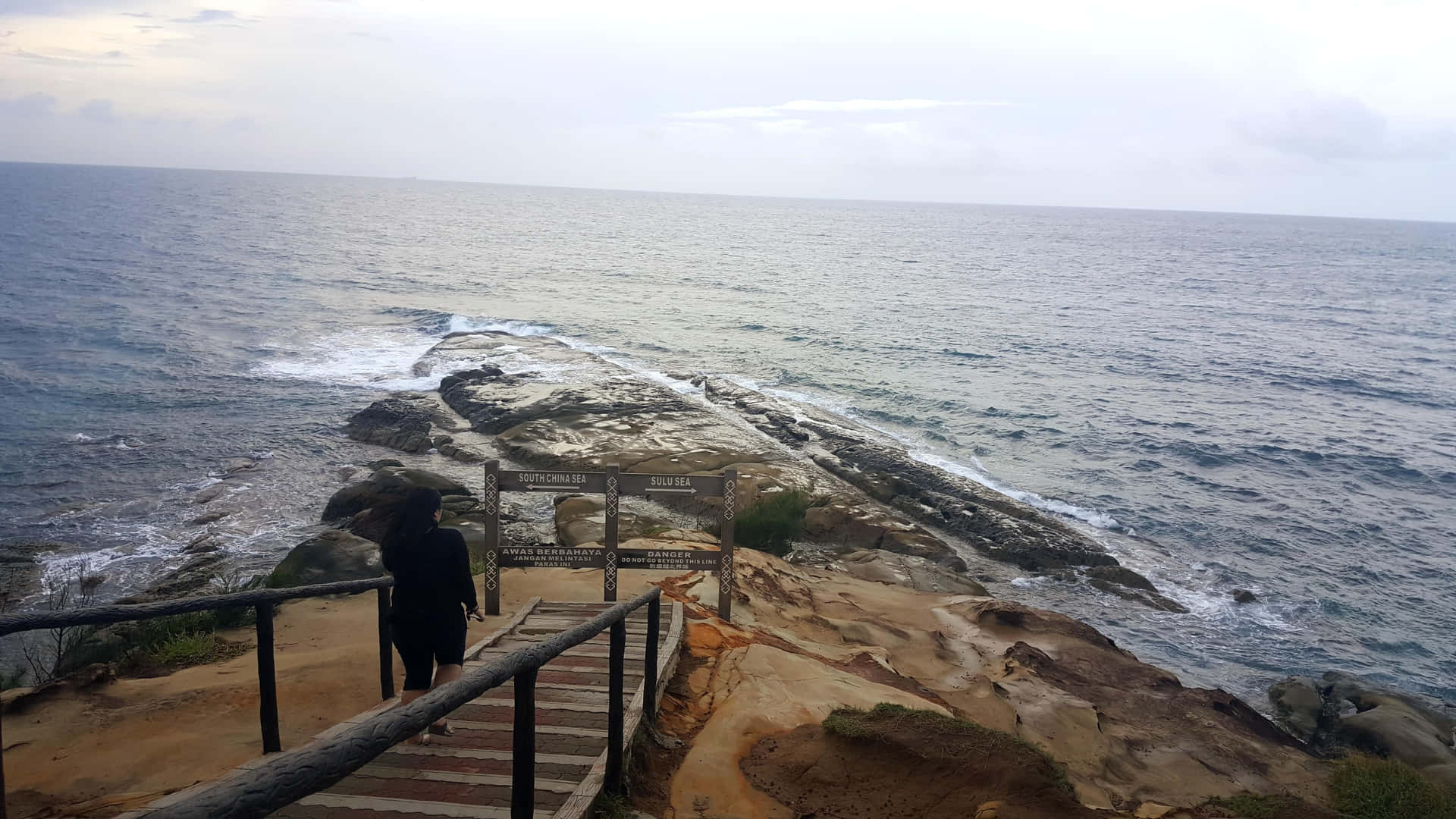 人物走下樓梯到岩石海邊，下方有海浪拍打。