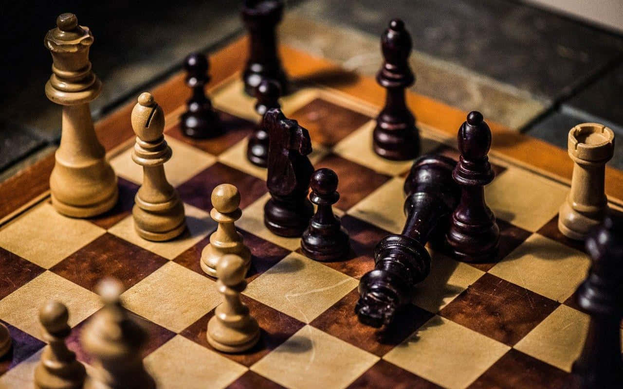 國際象棋 桌布 壁紙 — 木製國際象棋棋子喺棋盤上嘅特寫，有倒下嘅棋子顯示緊一場激烈嘅比賽進行中。