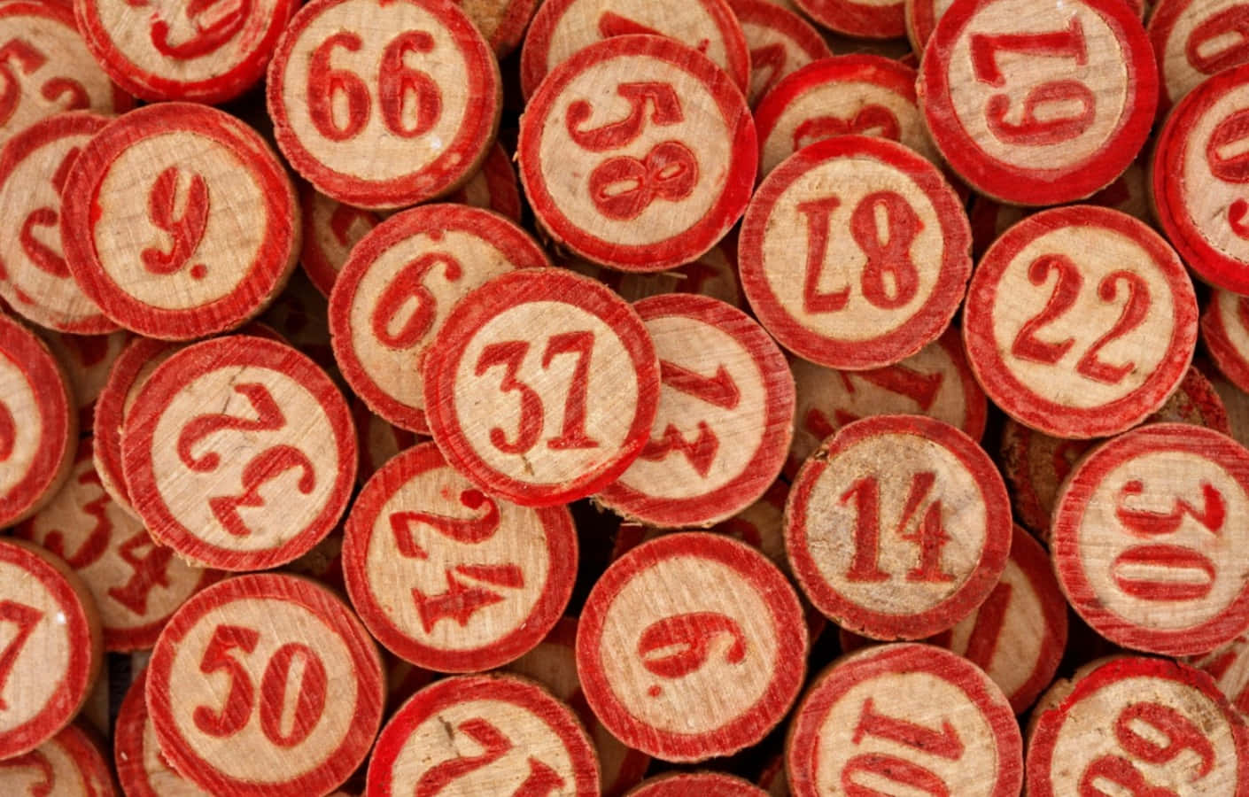 Bingo 桌布 壁紙 — 木製圓盤近距離特寫，上面有紅色雕刻數字，散落在有紋理的堆疊中。