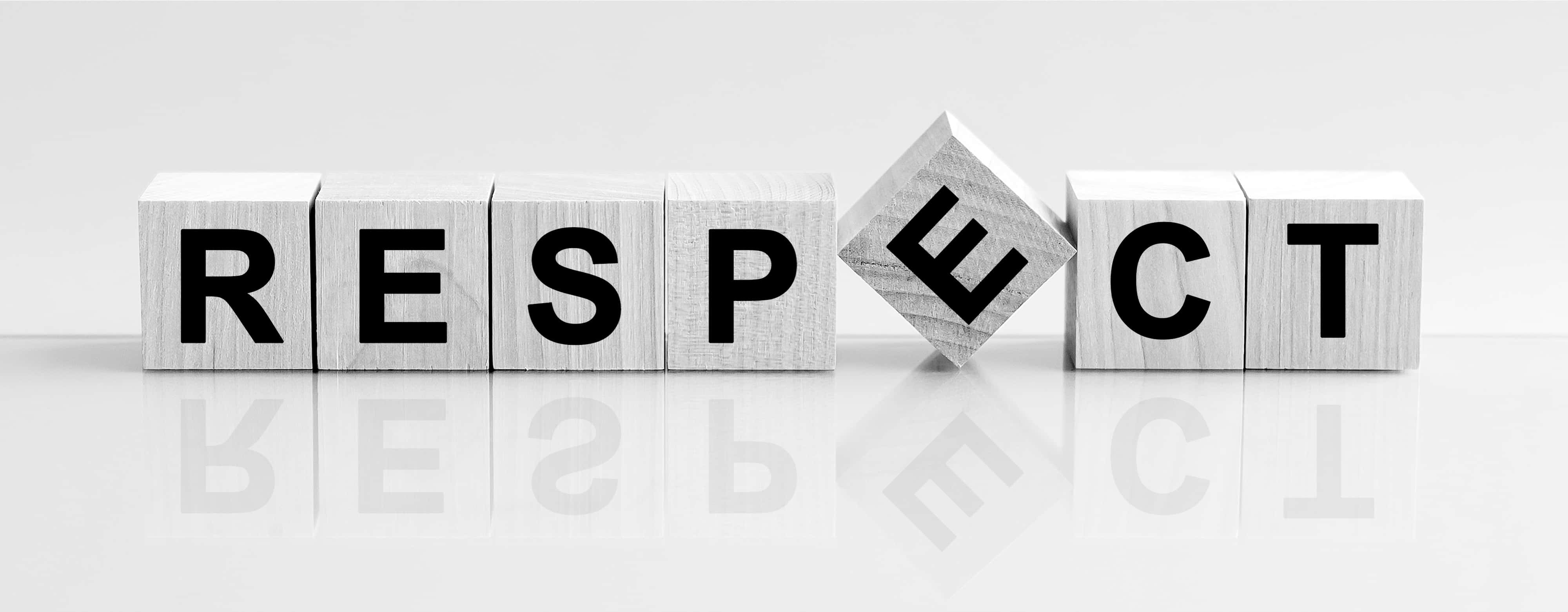木製字塊拼出「尊重」字樣 壁紙 — 木製積木拼出 RESPECT，其中 'E' 傾斜，在光滑的白色表面上投射倒影。