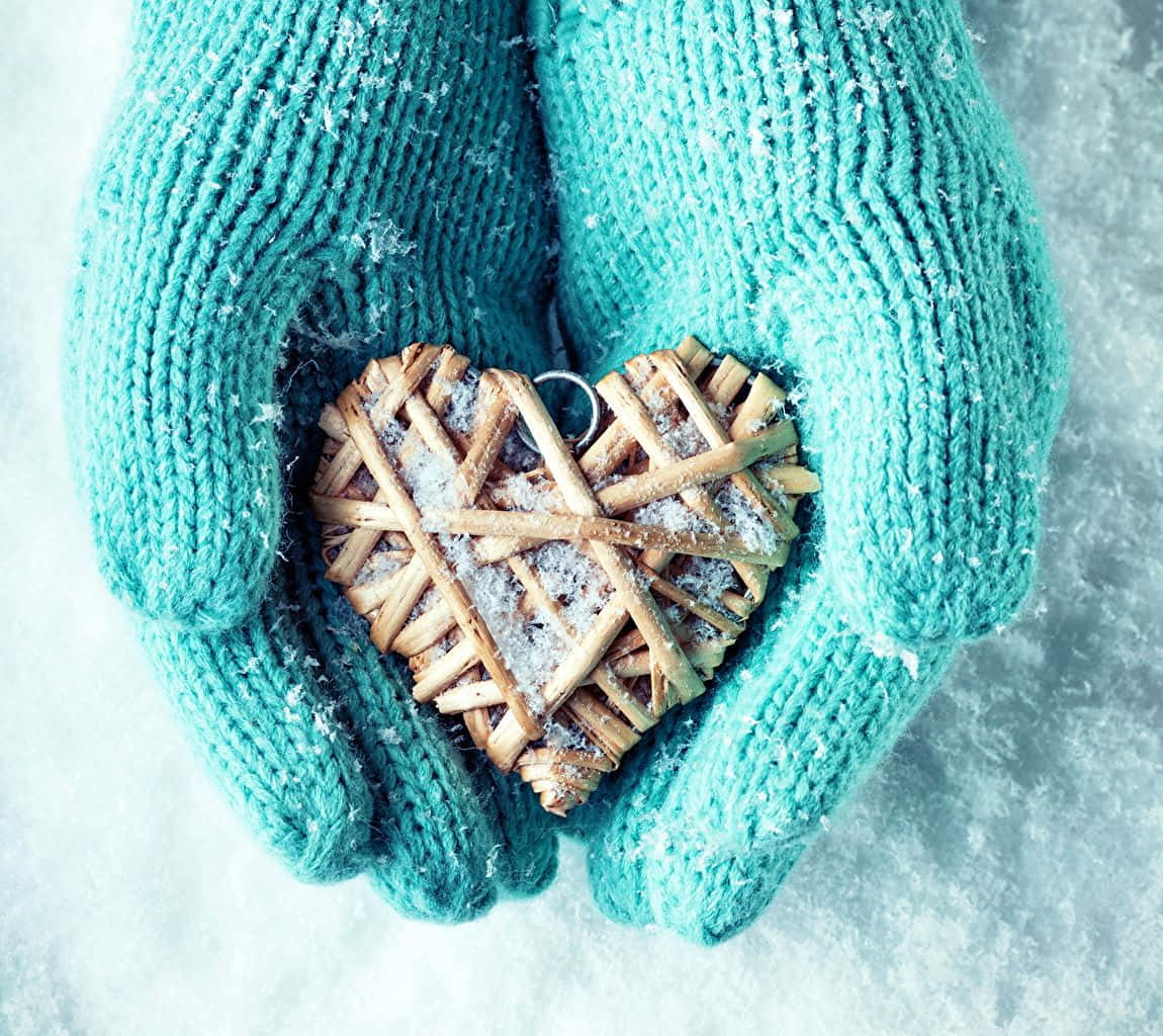 青綠色針織手套在冬日雪中捧著一個積雪編織的心形。
