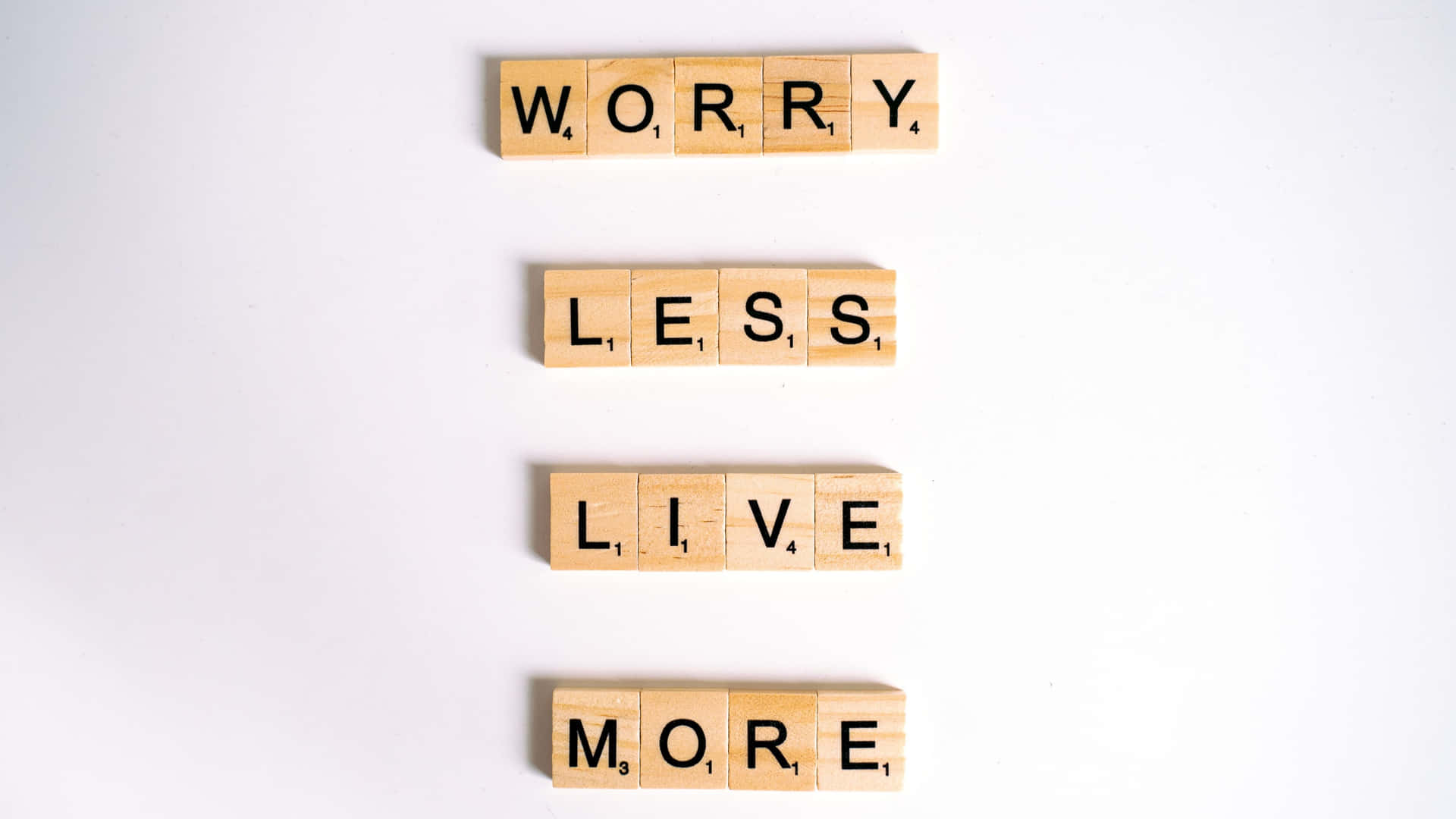 木製 Scrabble 字塊垂直排列，拼出 worry less live more。