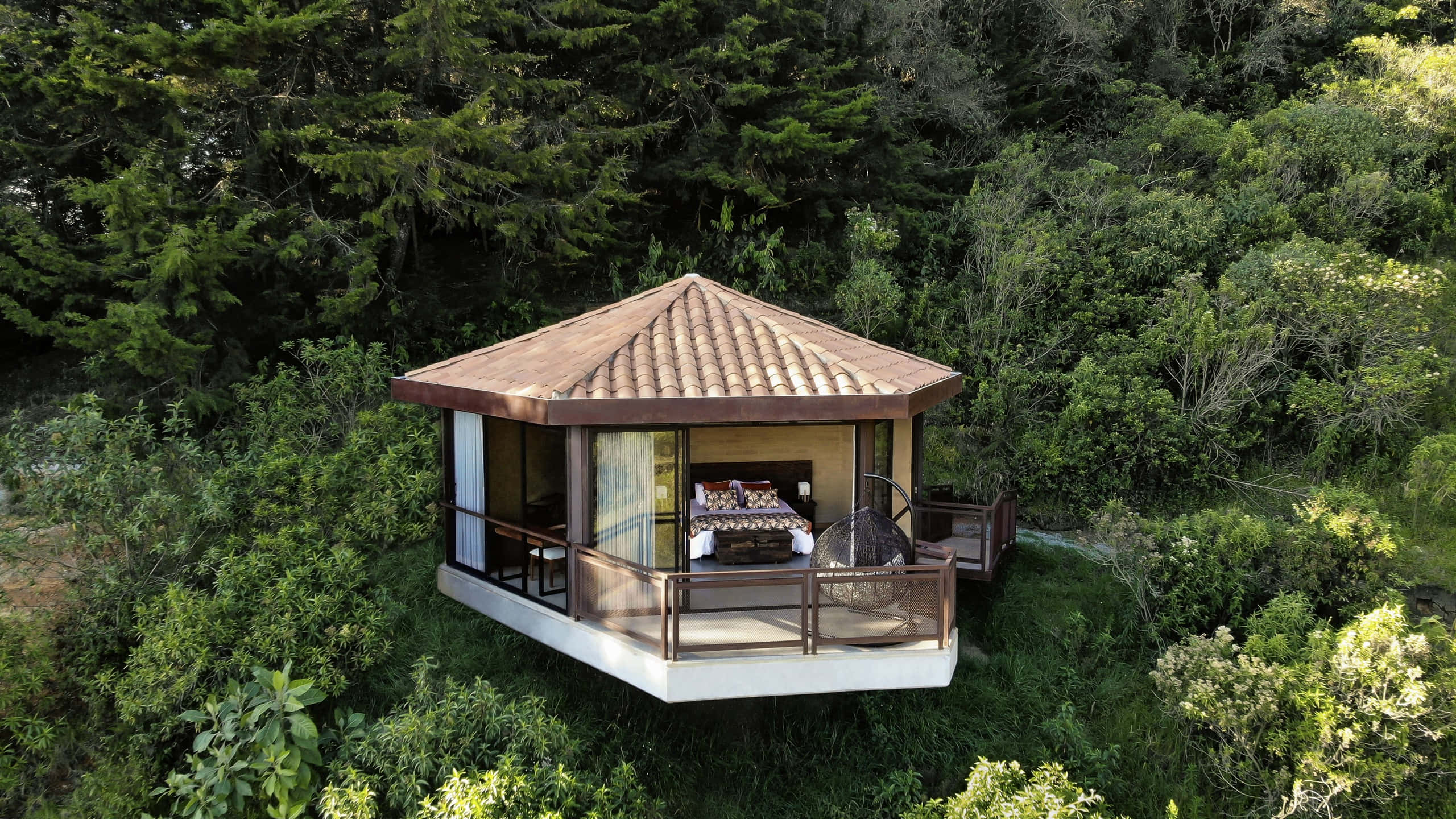 Eco-tourism 桌布 壁紙 — 木製樹屋別墅的鳥瞰圖，坐落在茂密的綠色森林中，設有開放式陽台和可見的室內床。