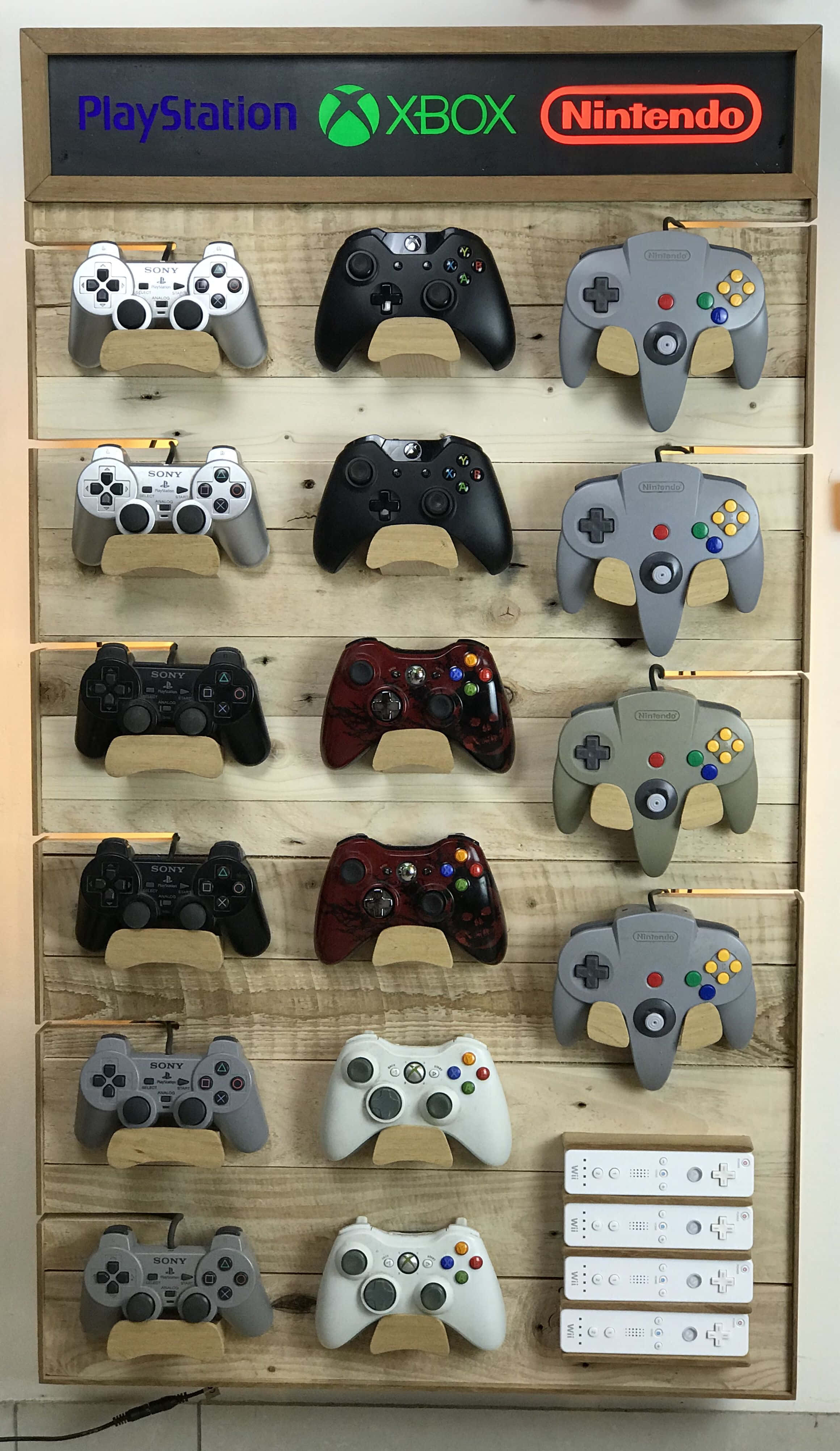 Game Console Emulators 桌布 壁紙 — 木製牆上展示架，整齊排列著復古PlayStation、Xbox和Nintendo遊戲控制器，上方有品牌標誌。