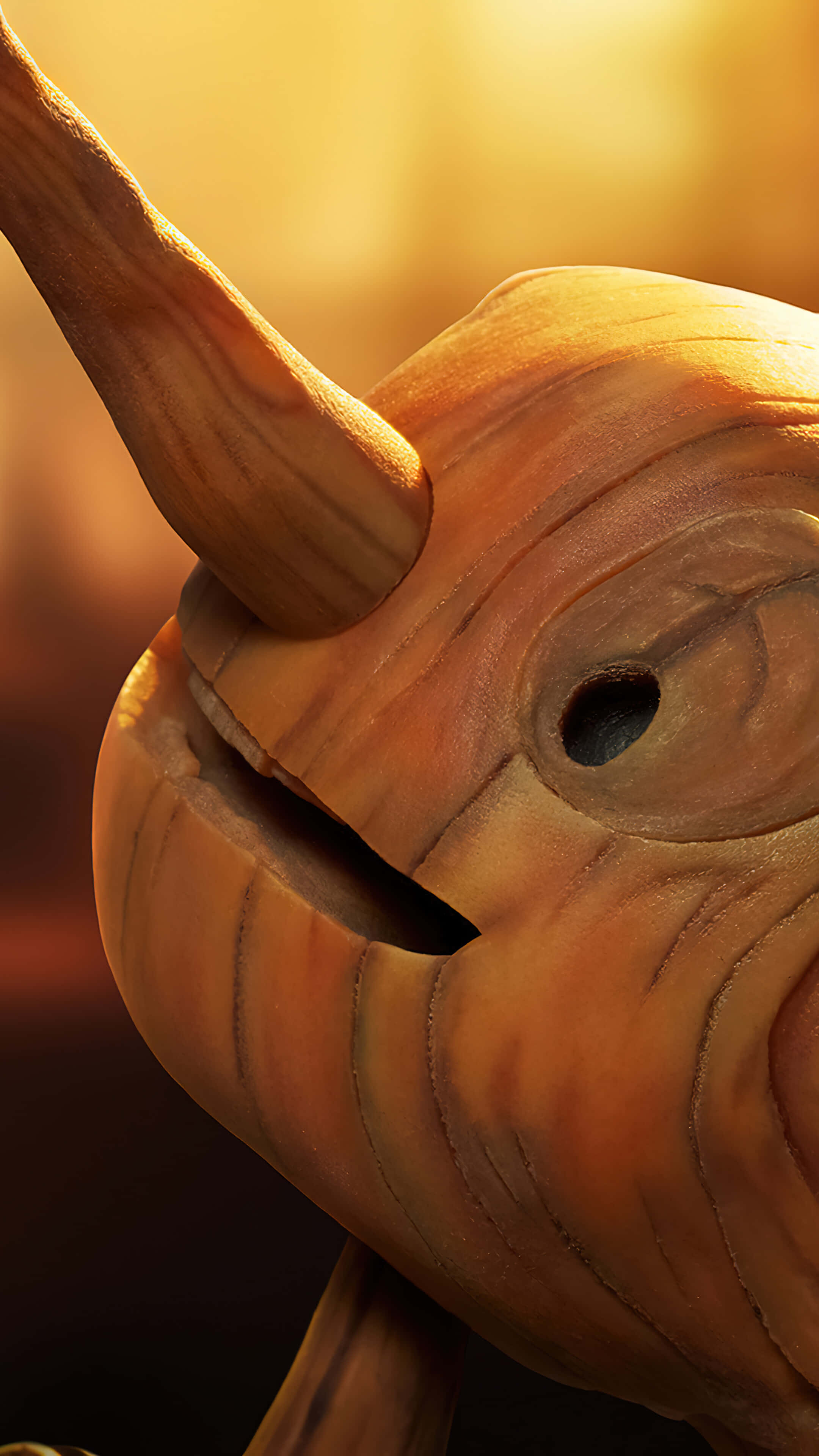Guillermo Del Toro's Pinocchio 桌布 壁紙 — 木製獨角鯨雕塑的特寫，溫暖的金色燈光突顯其紋理表面和彎曲的長牙。