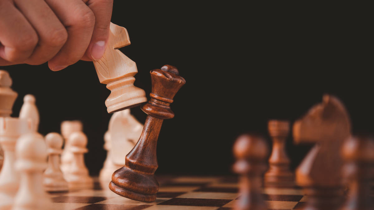 木製皇后對抗騎士 壁紙 — 一隻手舉起白色兵棋，在黑色背景的棋盤上吃掉黑色王棋。