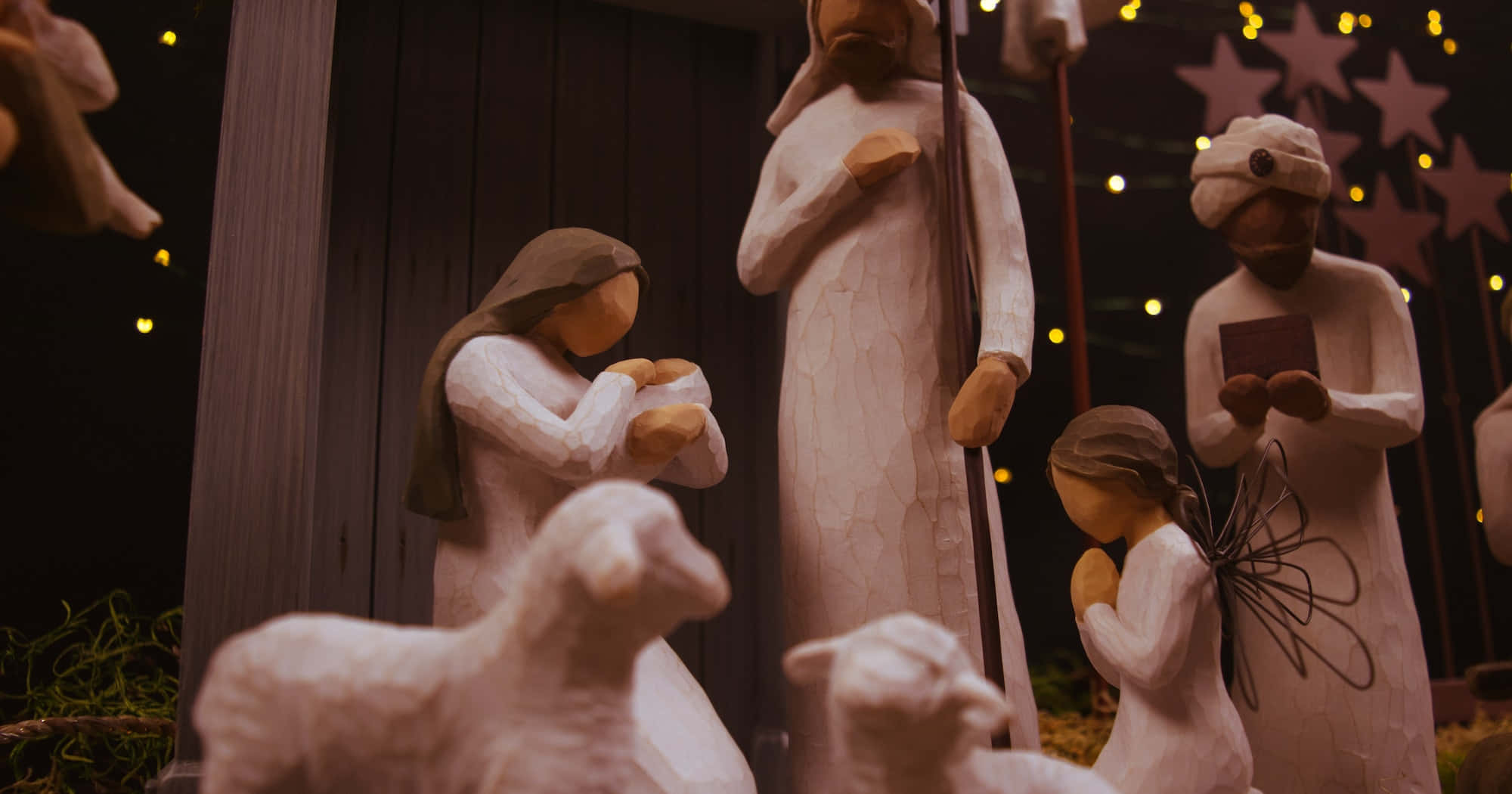 Nativity Scene 桌布 壁紙 — 木製耶穌誕生人偶在星形裝飾的黑暗背景下，在燈串下溫暖地發光。