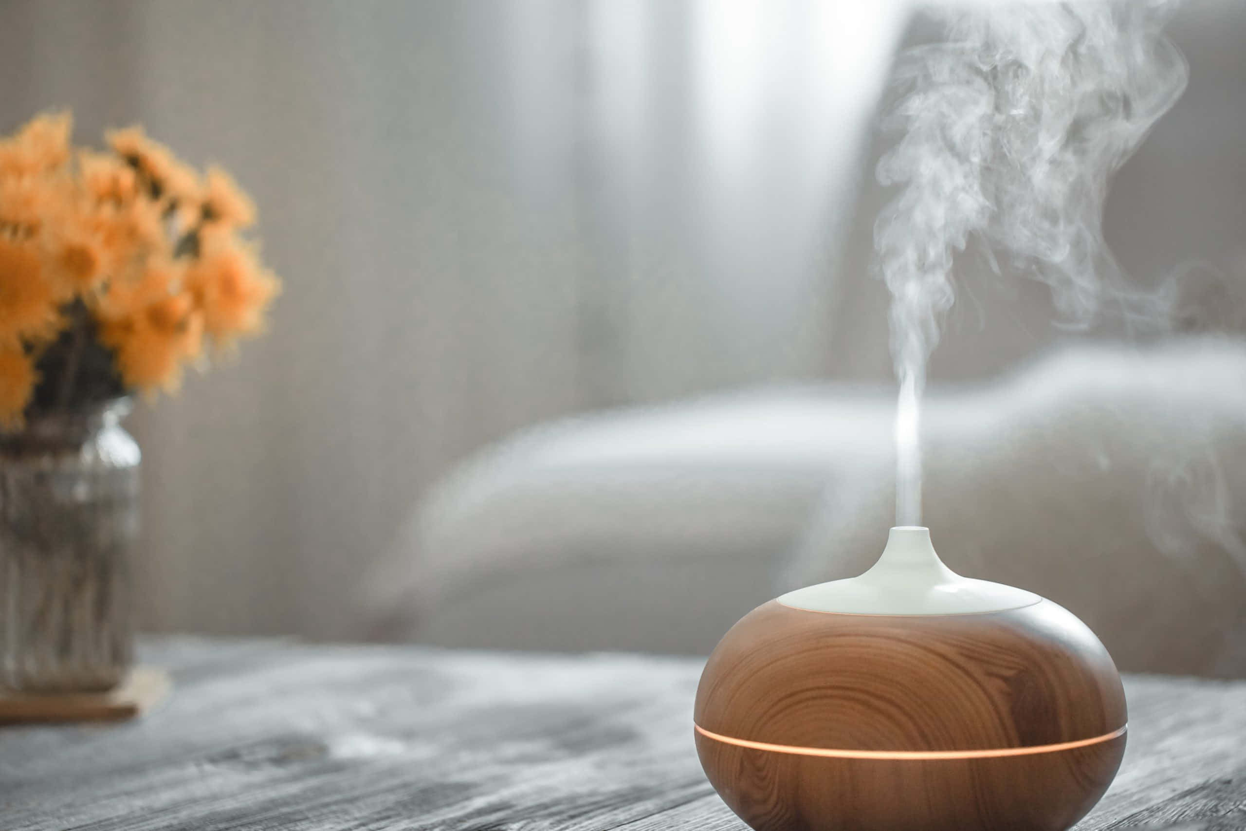 Aromatherapy 桌布 壁紙 — 木製香薰機在一個鄉村風格的桌子上，旁邊放著一瓶橙色花，散發出柔和的水霧。