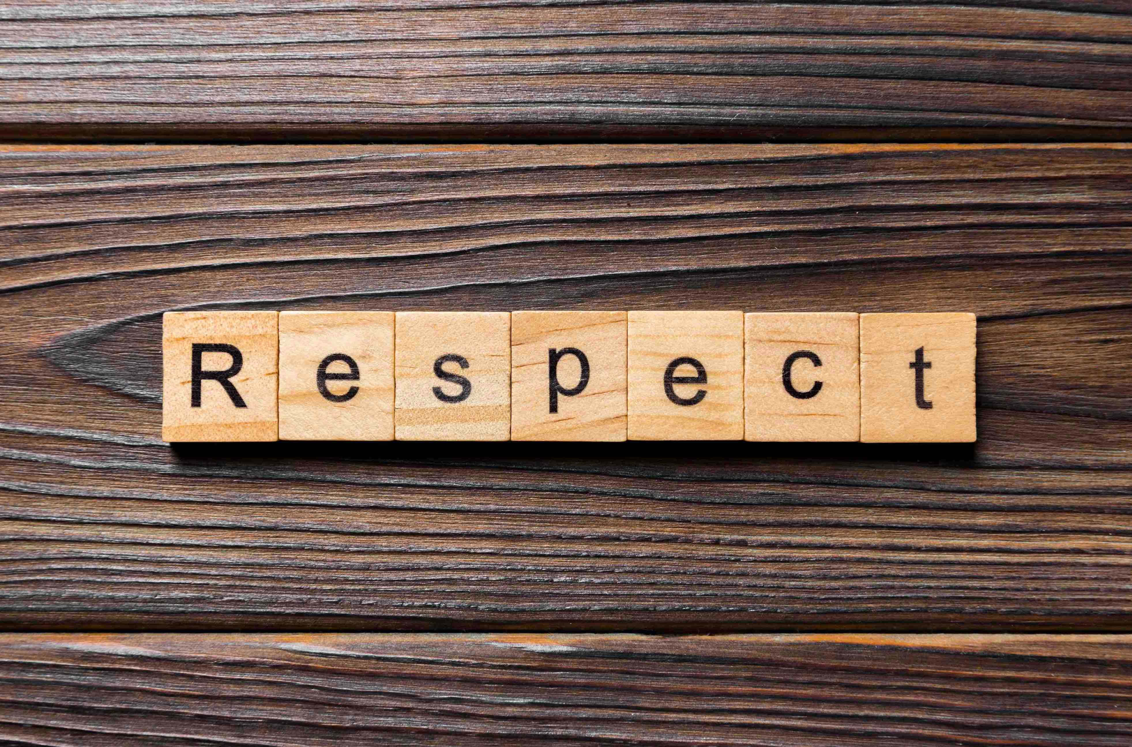 木質背景上拼寫出的「尊重」字樣 壁紙 — 用木製字母瓷磚拼寫的「Respect」一詞，放置在深色紋理木質表面上。