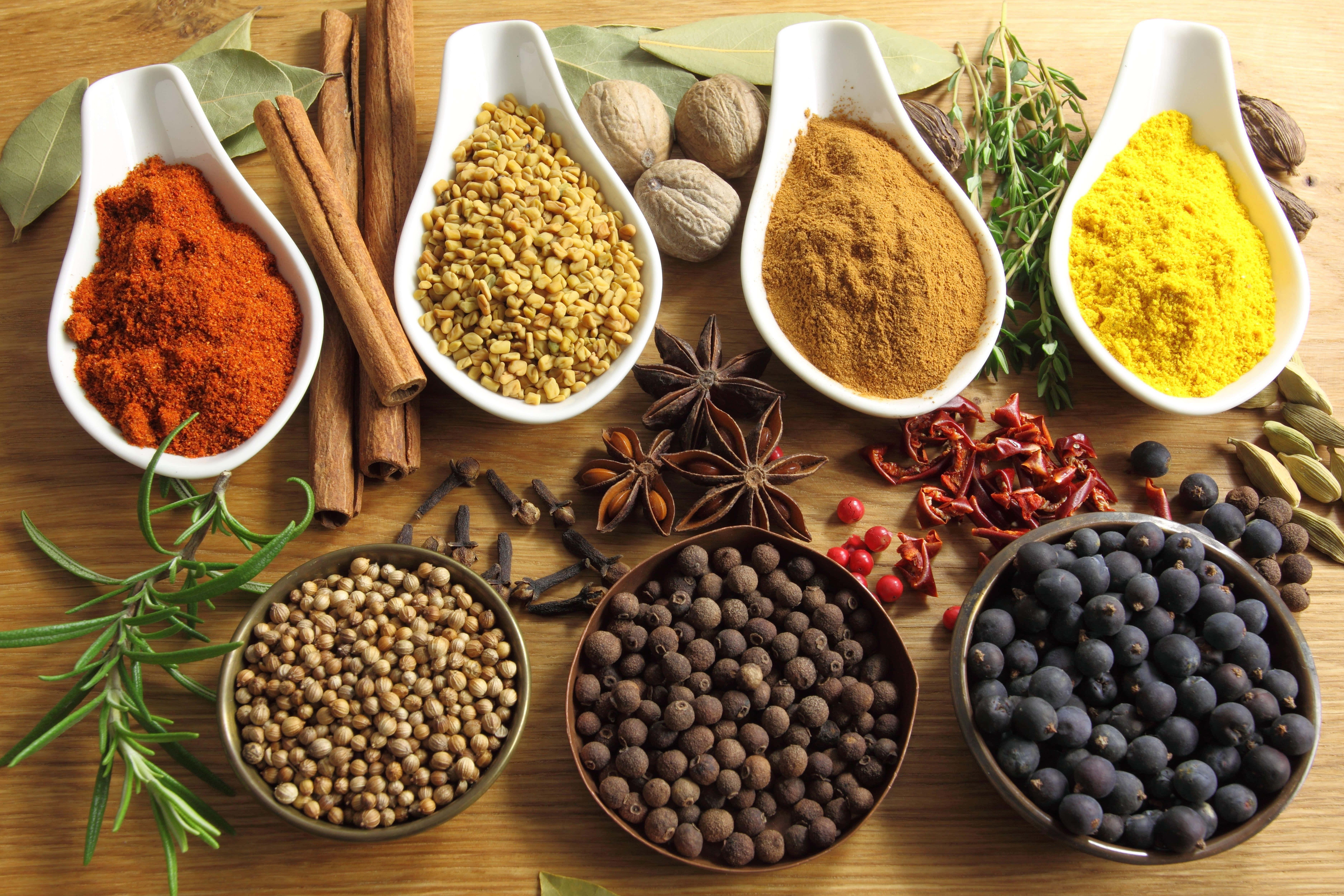 Spices 桌布 壁紙 — 木質表面上白色湯匙和碗中擺放的鮮豔香料和香草陣列。