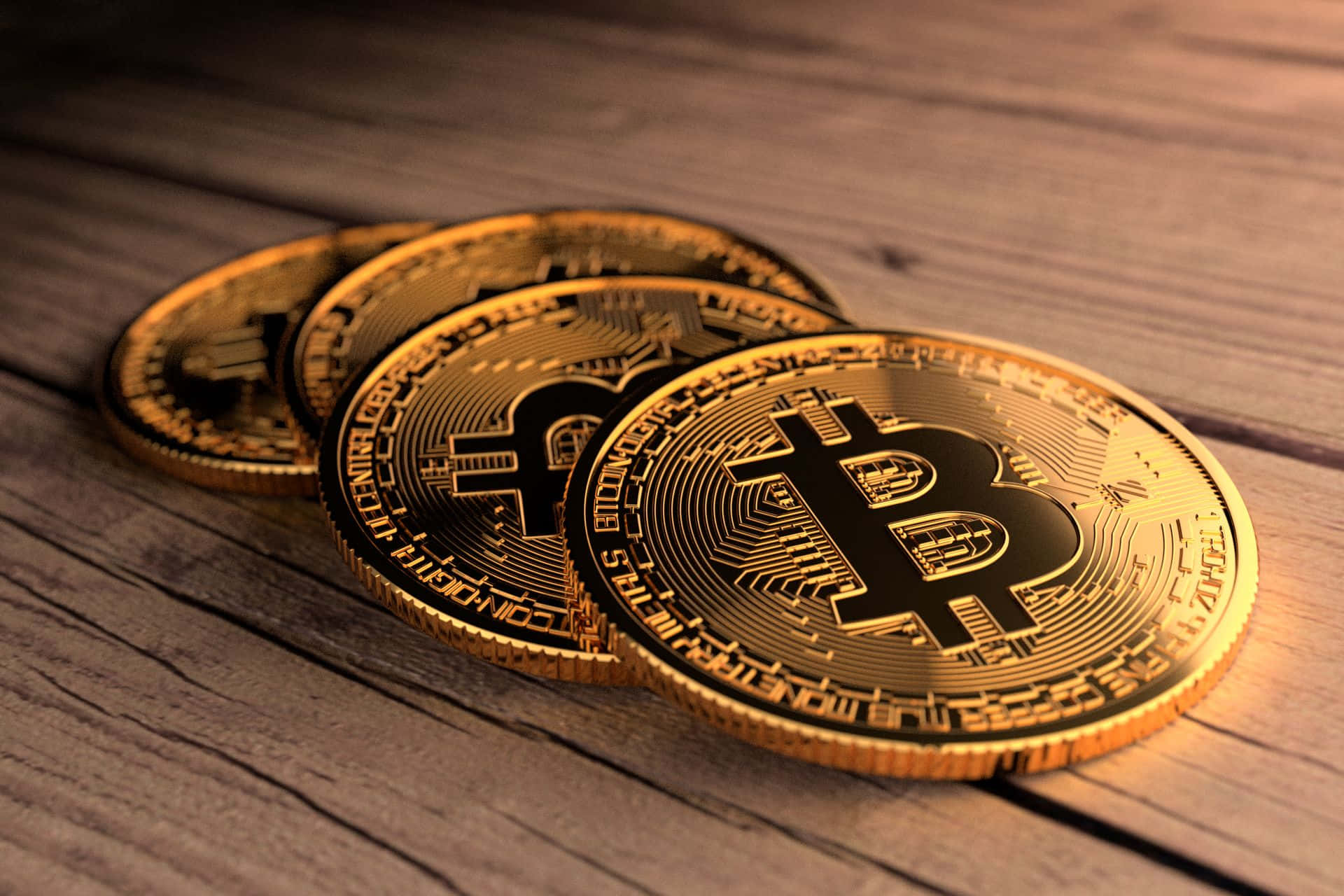 未來的數位貨幣——比特幣 壁紙 — 四枚閃閃發光的金色比特幣以對角線堆疊在經風化的木質表面上，在溫暖的燈光下。