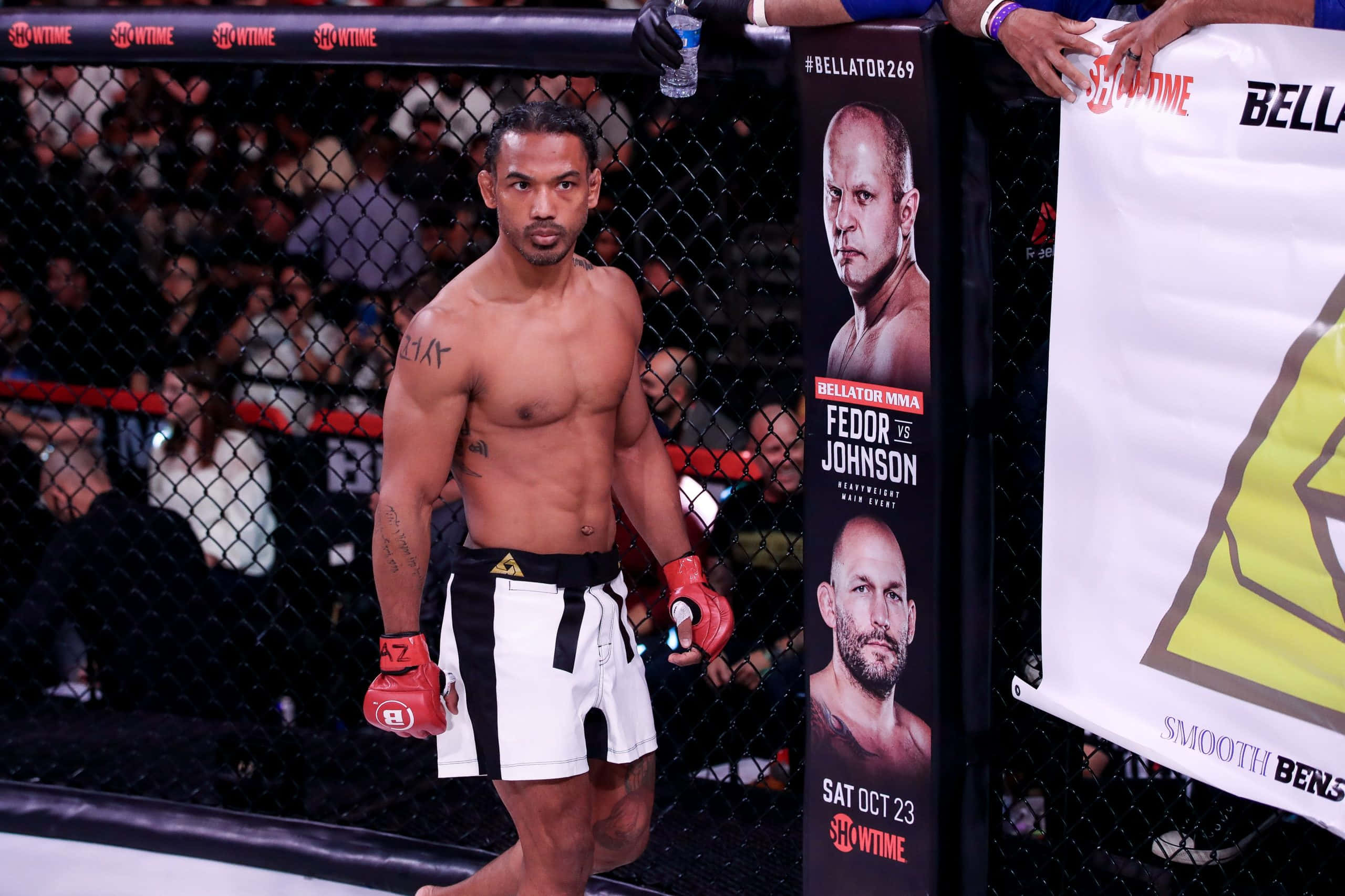 本·亨德森，Bellator Promotions 賽事 壁紙 — 一位肌肉發達的MMA拳手，戴著紅色手套，穿著黑白短褲，站在八角籠內，圍欄後面有群眾。